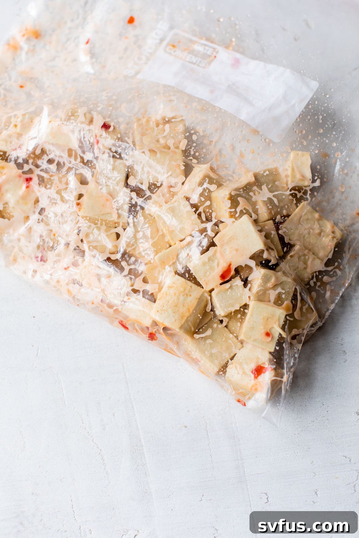 Cubed tofu marinating in a plastic bag with sweet chili sauce and cornstarch, ready for frying.