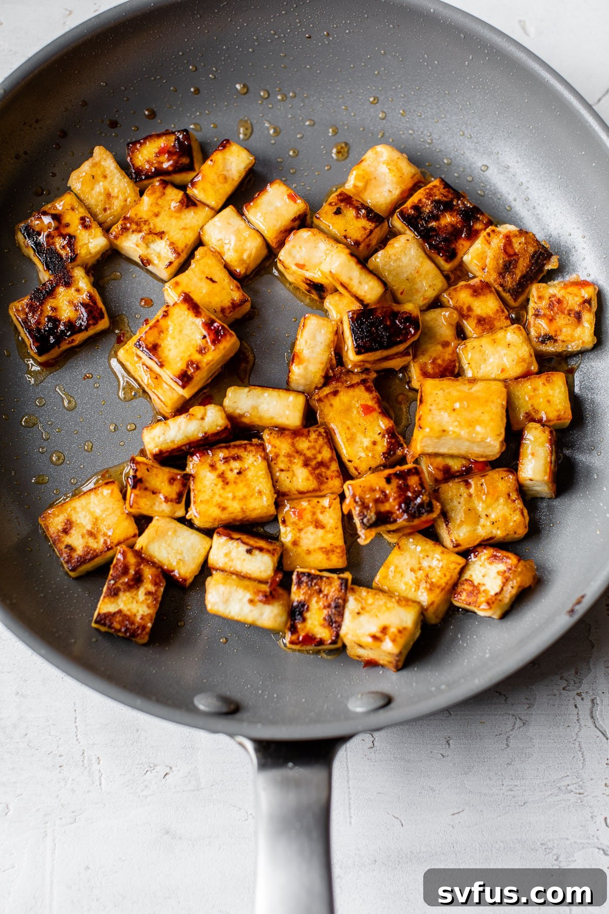 Crispy pan-fried tofu cubes sizzling in a skillet, turning golden brown and developing a delicious crust.