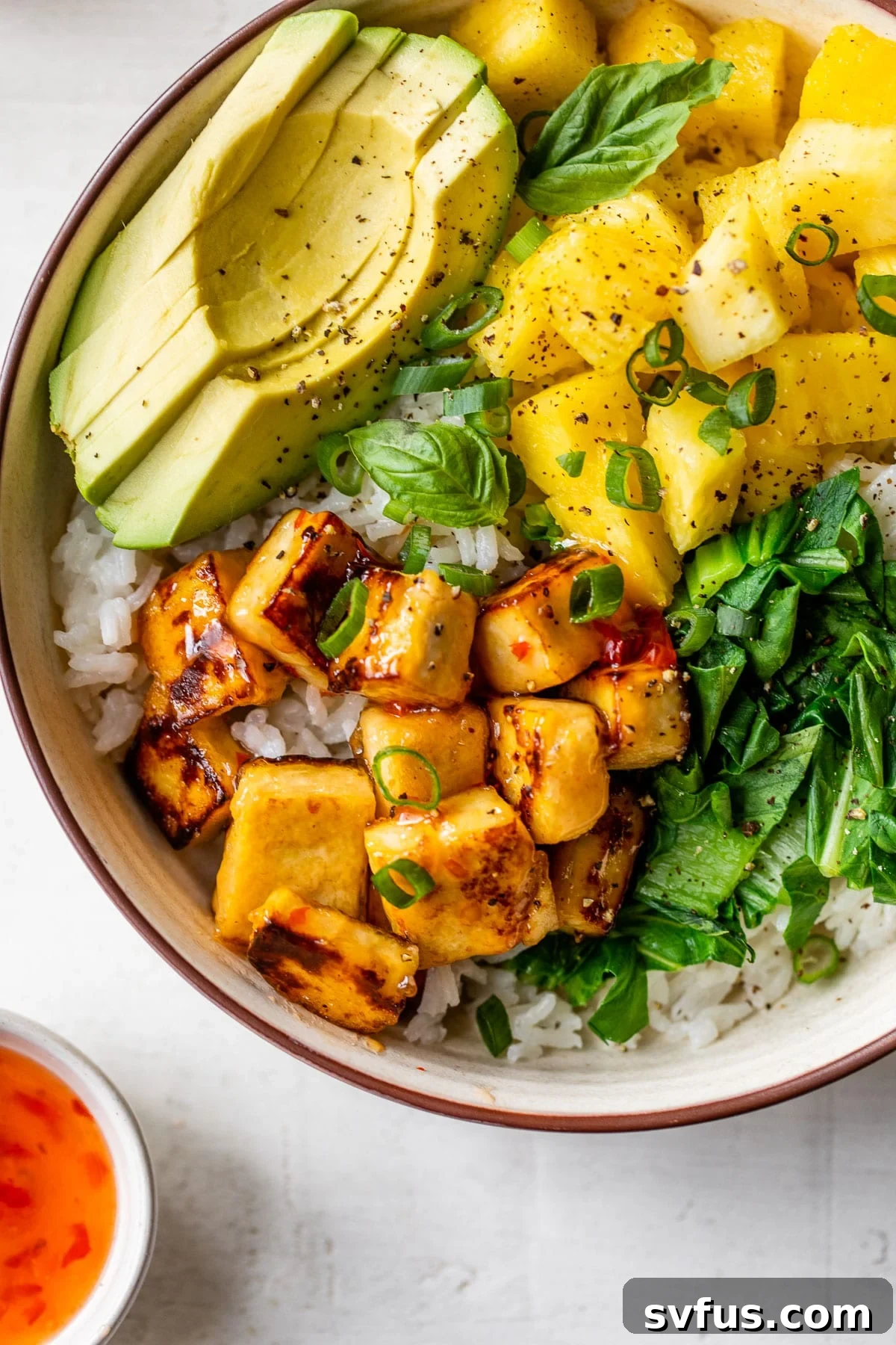 Close-up photo of crispy golden tofu cubes nestled in a bowl with fluffy rice and perfectly sliced avocado, highlighting the textures and colors of the meal.