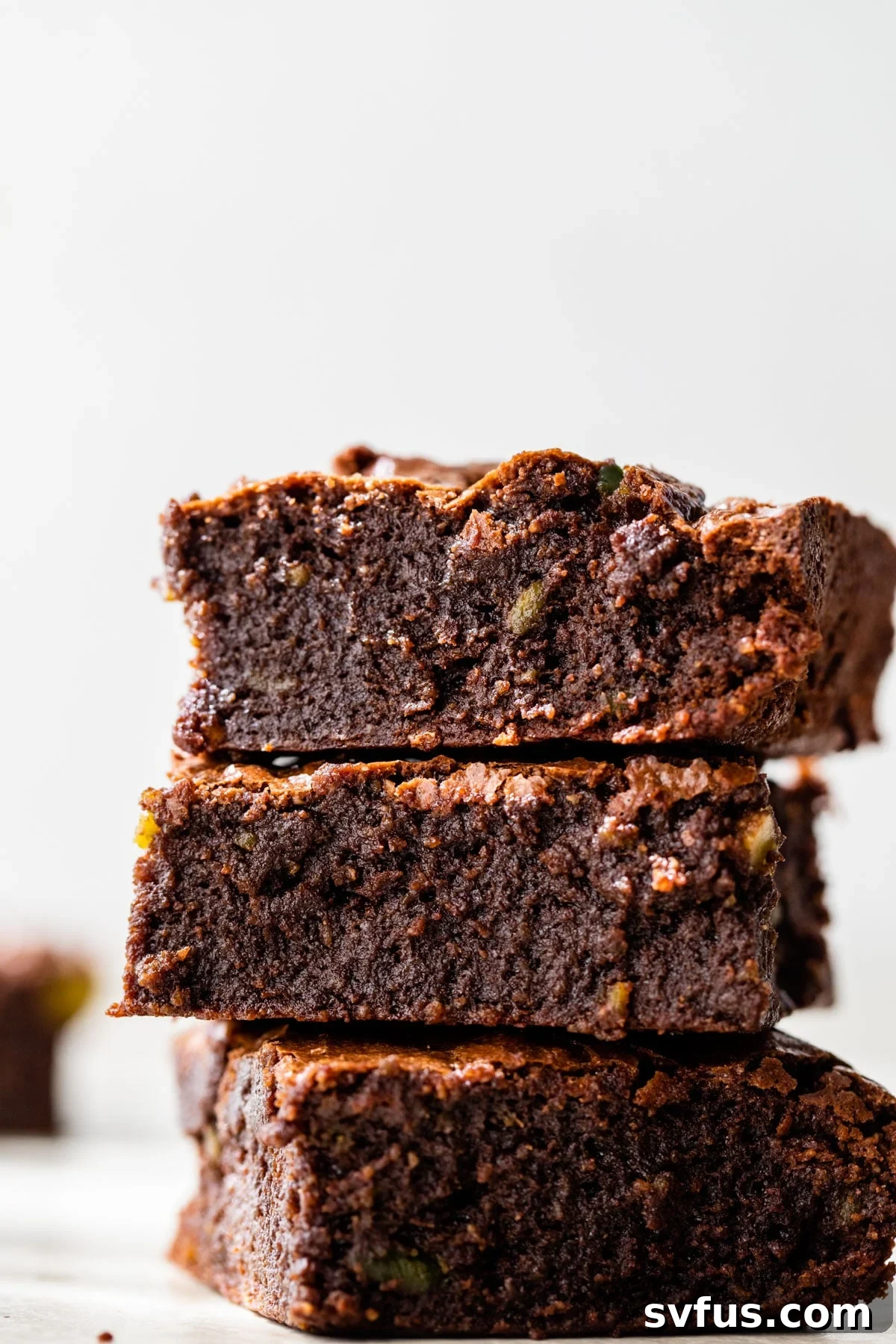 A stack of three rich, fudgy avocado brownies with a perfectly crackled top, hinting at their decadent texture.