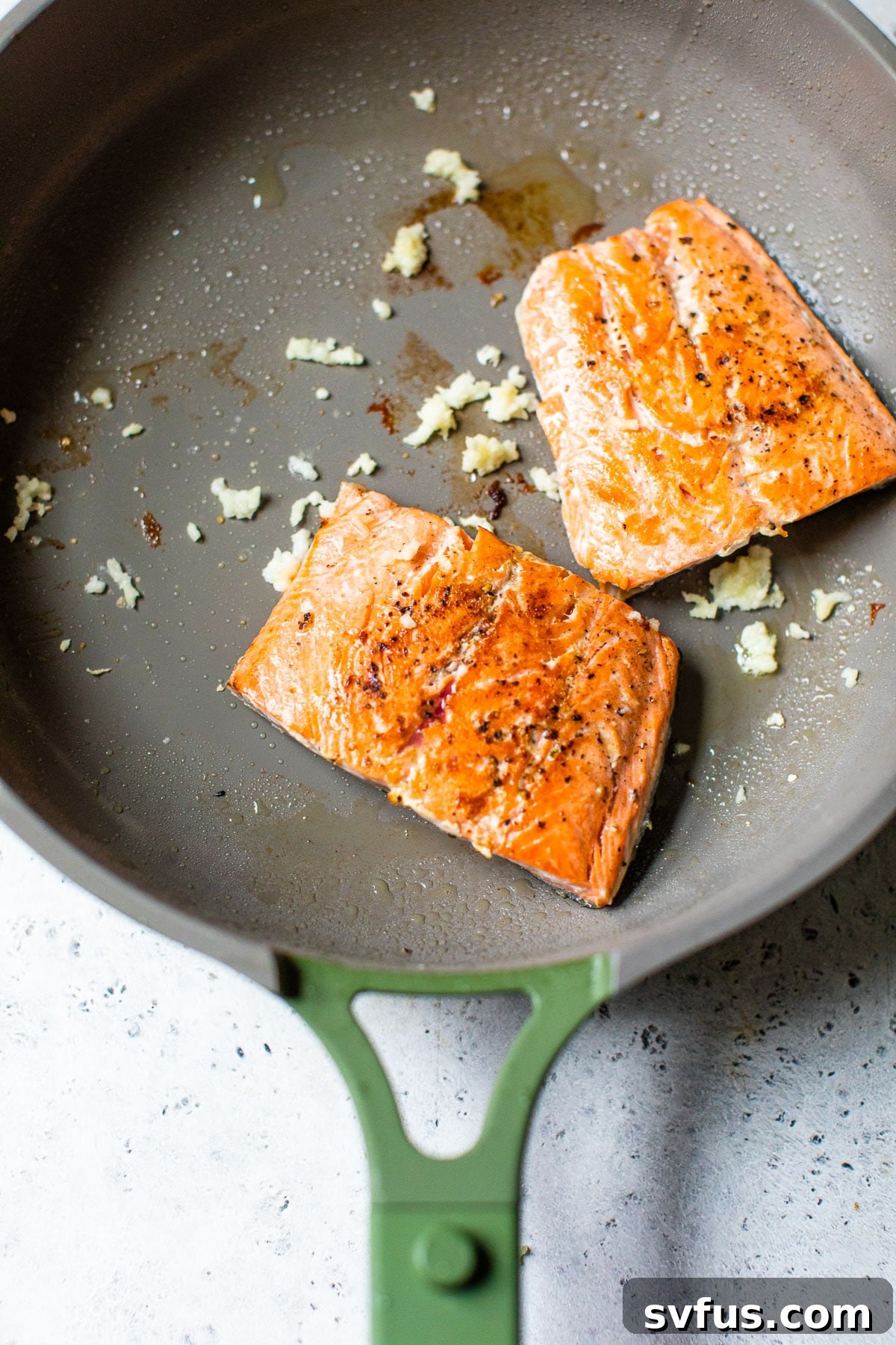 Close-up of seared salmon fillets with fragrant minced garlic in a nonstick skillet