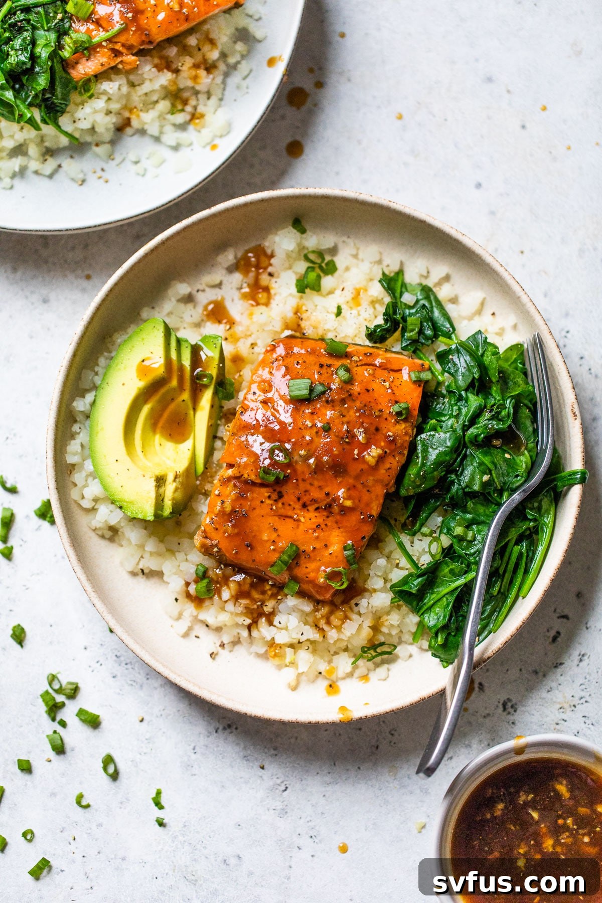 A vibrant and satisfying bowl featuring perfectly cooked teriyaki-glazed salmon, fluffy cauliflower rice, sautéed spinach, and creamy avocado slices, garnished with fresh green onions