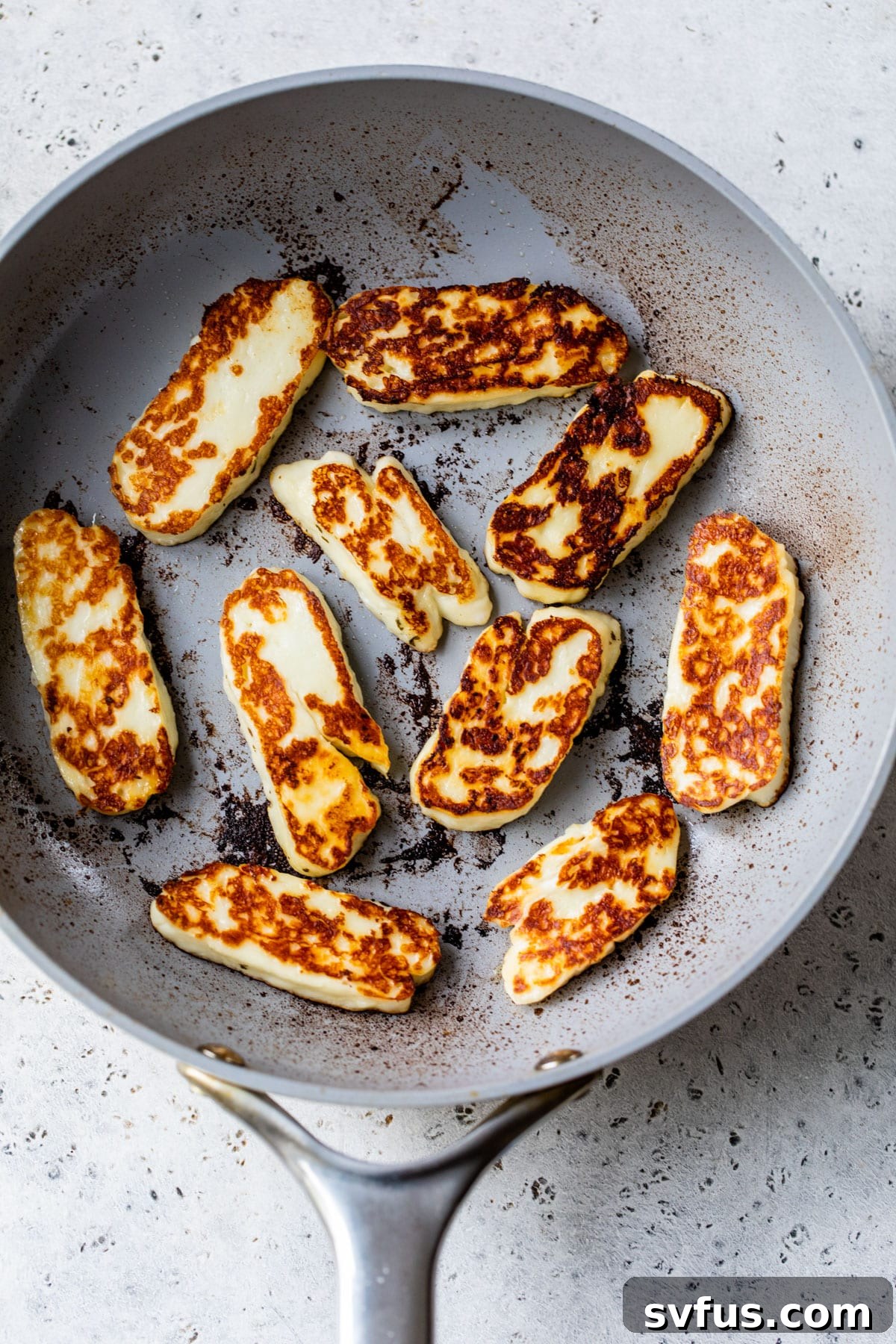 Close-up view of golden-brown, perfectly pan-fried halloumi slices sizzling in a hot skillet, showcasing their delicious crispy exterior.