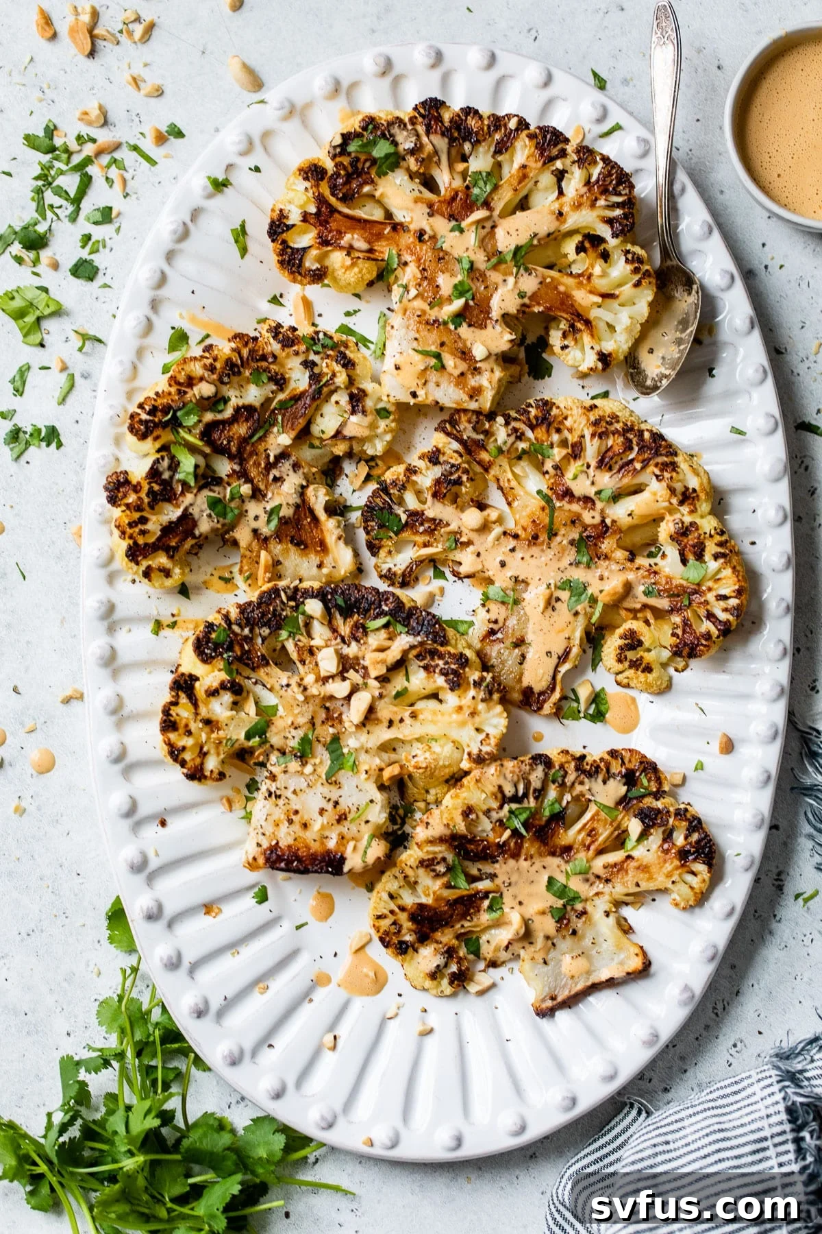 Five roasted cauliflower steaks arranged on a large serving platter, drizzled with peanut sauce.
