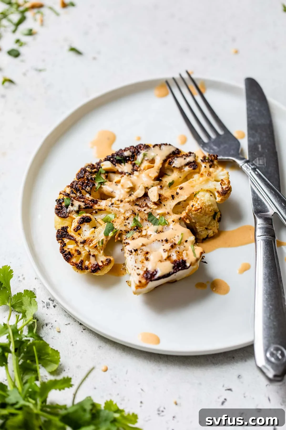 A roasted cauliflower steak on a plate with a fork and knife, ready to eat.