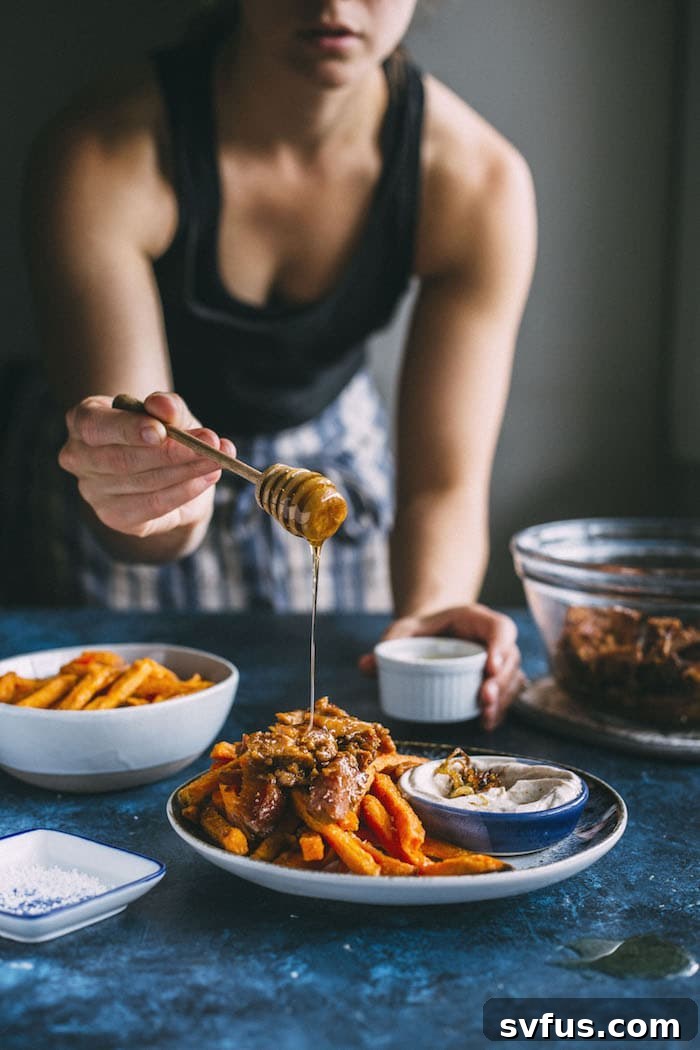 Close-up of golden sweet potato fries generously topped with tender honey ginger pork and a drizzle of creamy dip.