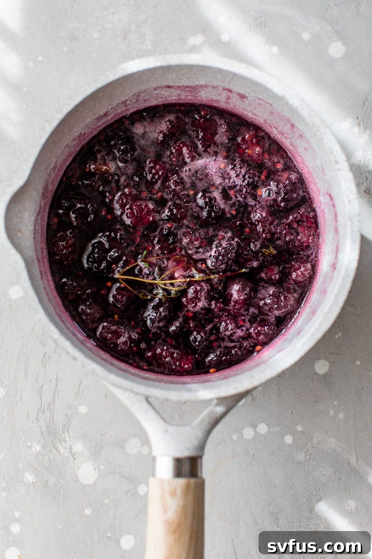 blackberry simple syrup in a small saucepan, showing the berries being mashed