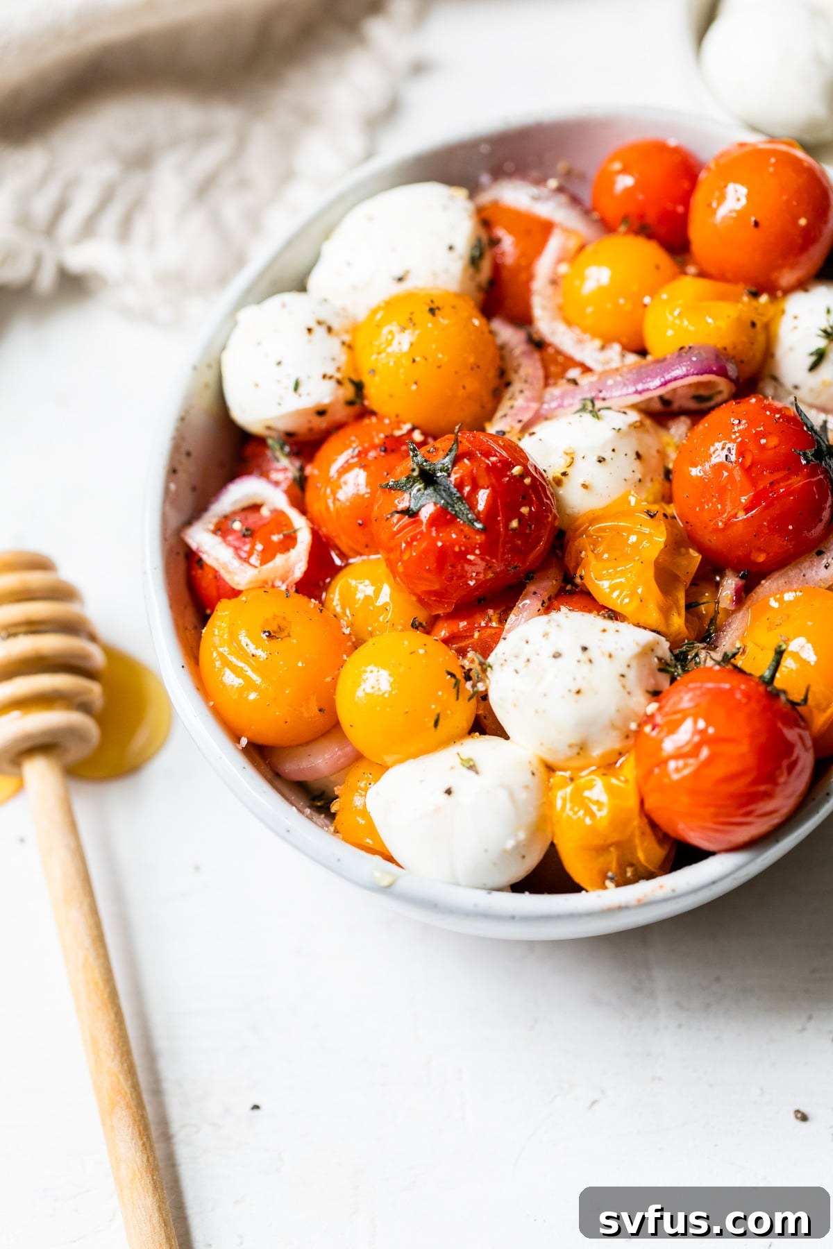 Close up of honey roasted tomatoes and mozzarella pearls, garnished with green herbs