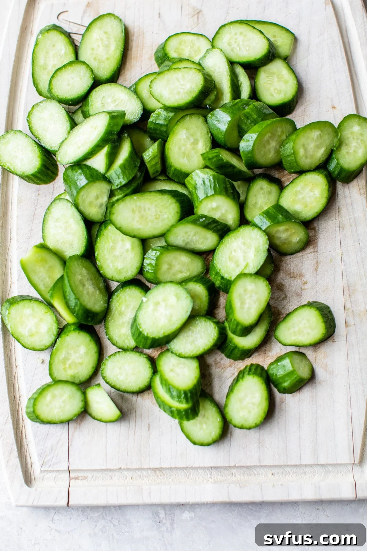 Freshly sliced cucumbers resting on a wooden cutting board, ready for the spicy dressing