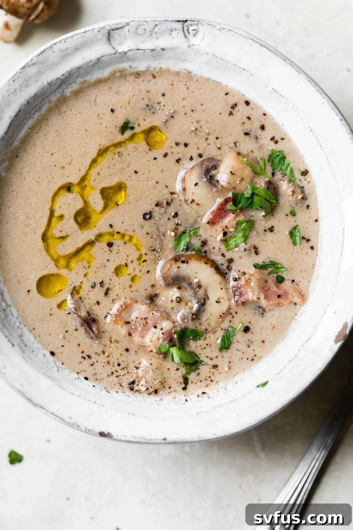 A beautifully presented bowl of creamy Whole30 mushroom soup, garnished with fresh herbs and crumbled bacon.