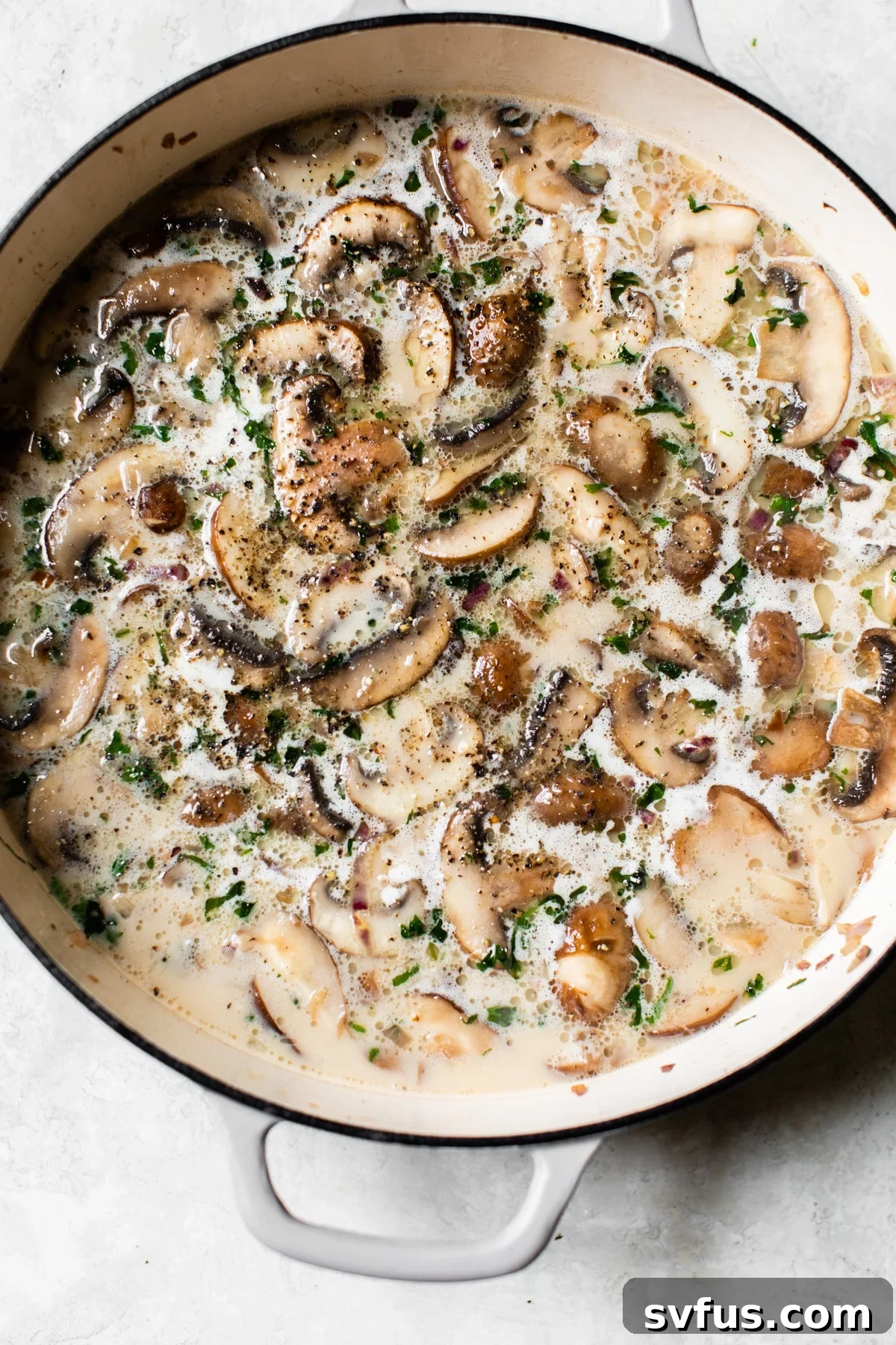 Chicken broth and creamy coconut milk being added to the sautéed mushrooms and shallots in a large pot, ready to simmer.