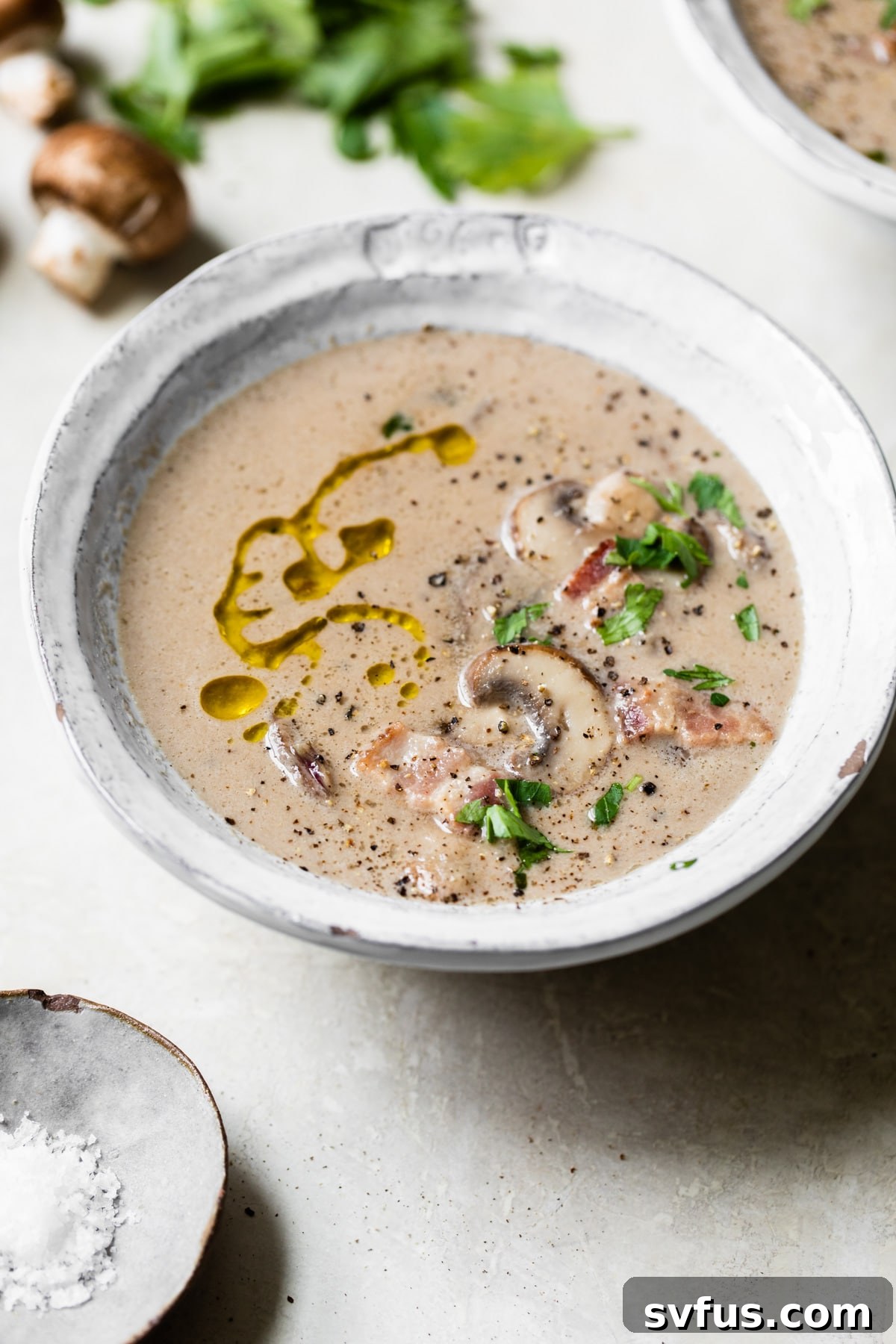 A close-up shot of a bowl of creamy Whole30 mushroom soup, garnished with fresh mushrooms and crispy bacon pieces.