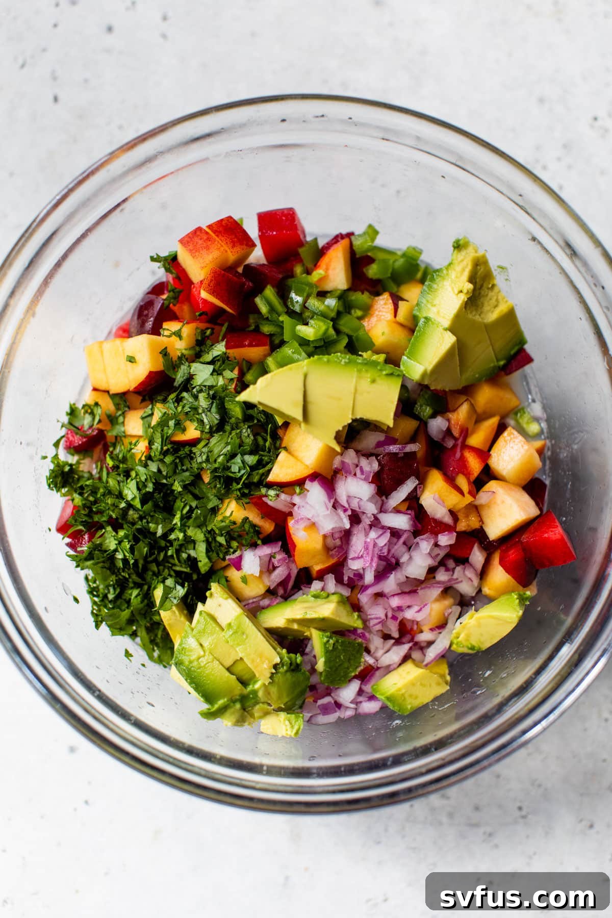 All the diced ingredients for Stone Fruit Ceviche – shrimp, peaches, nectarines, plum, red onion, jalapeño, cilantro, and avocado – are combined in a large glass bowl, creating a colorful and appetizing mix.