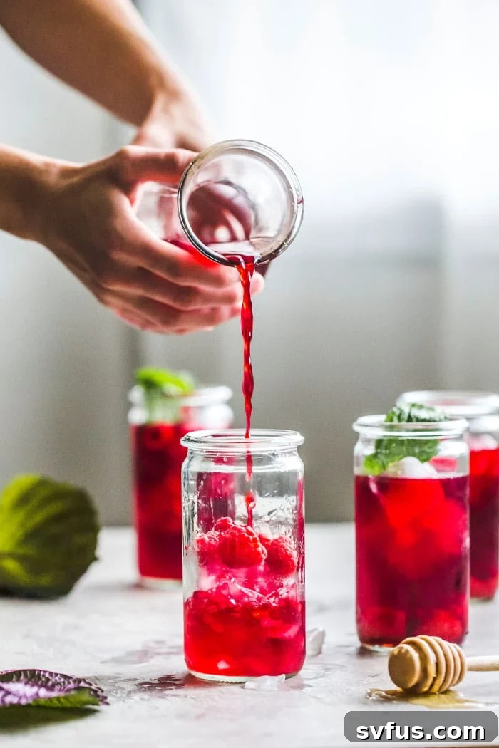Two glasses of Raspberry Hibiscus Iced Tea with fresh berries and mint sprigs.