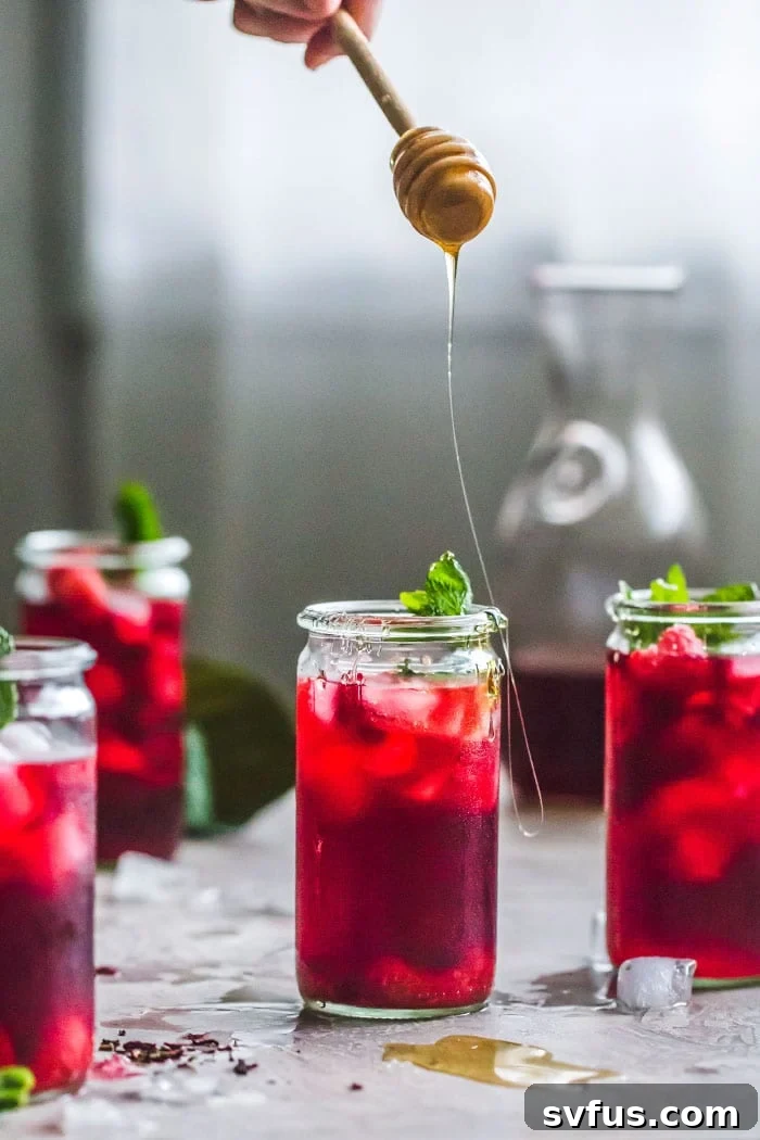 Close-up of a raspberry floating in a glass of hibiscus iced tea, with mint.