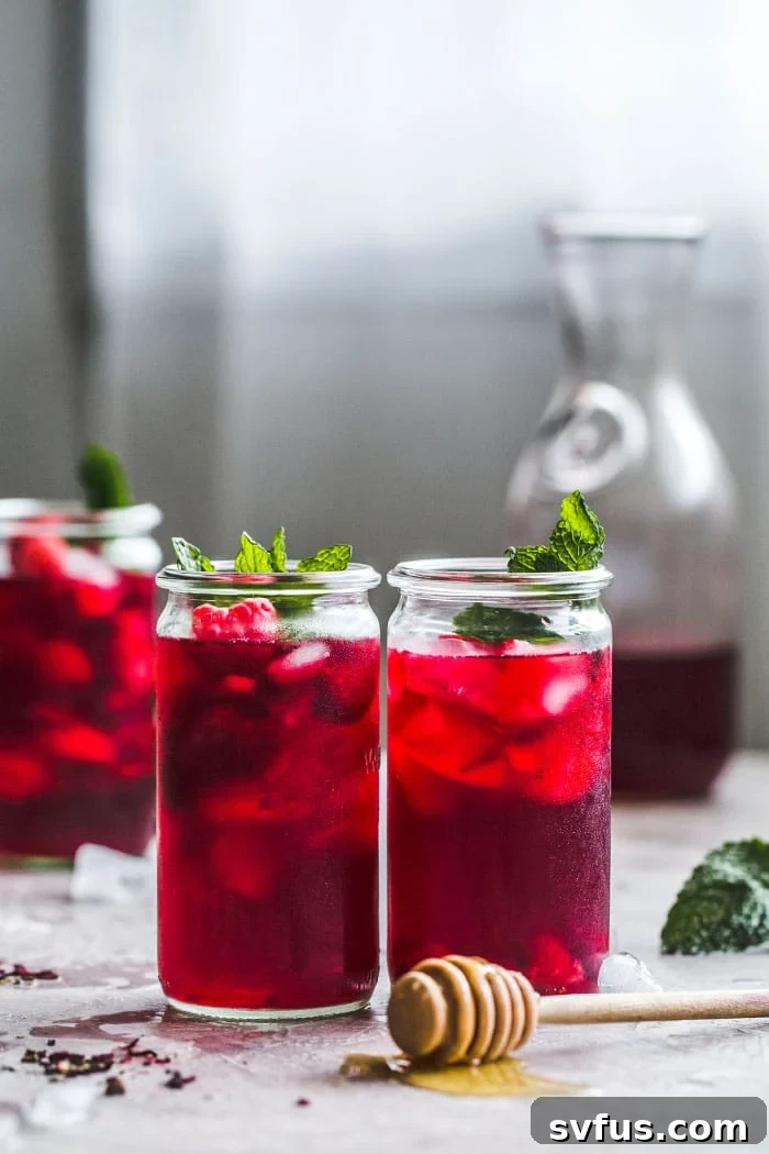 A pitcher filled with Raspberry Hibiscus Iced Tea, surrounded by fresh raspberries and mint.