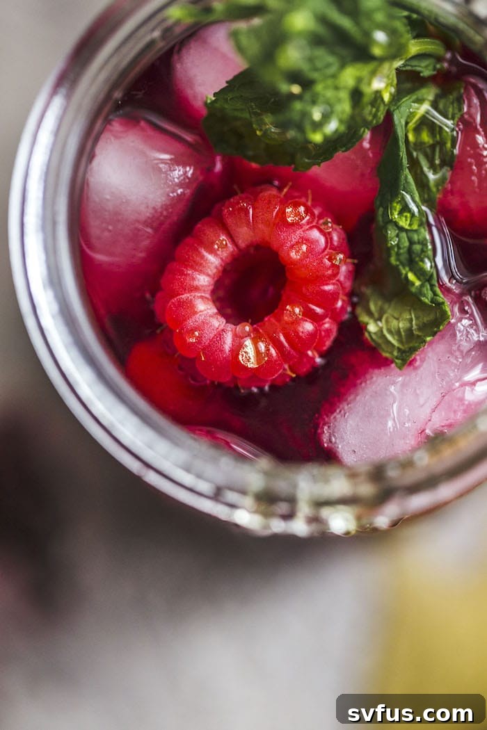 Close-up of a tea strainer pouring hibiscus tea into a glass pitcher.