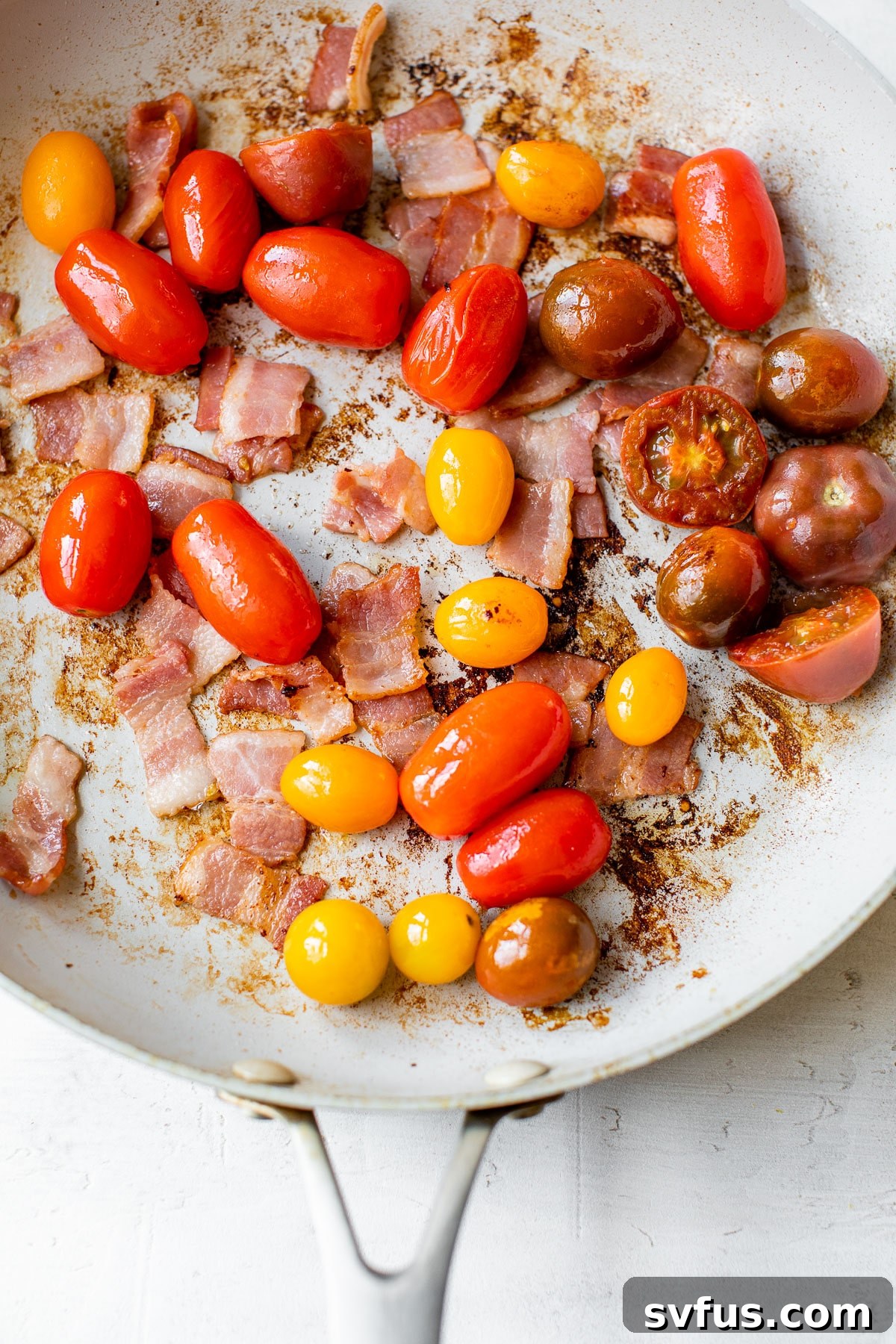 cooked bacon and grape tomatoes in a large skillet, ready for the zucchini noodles