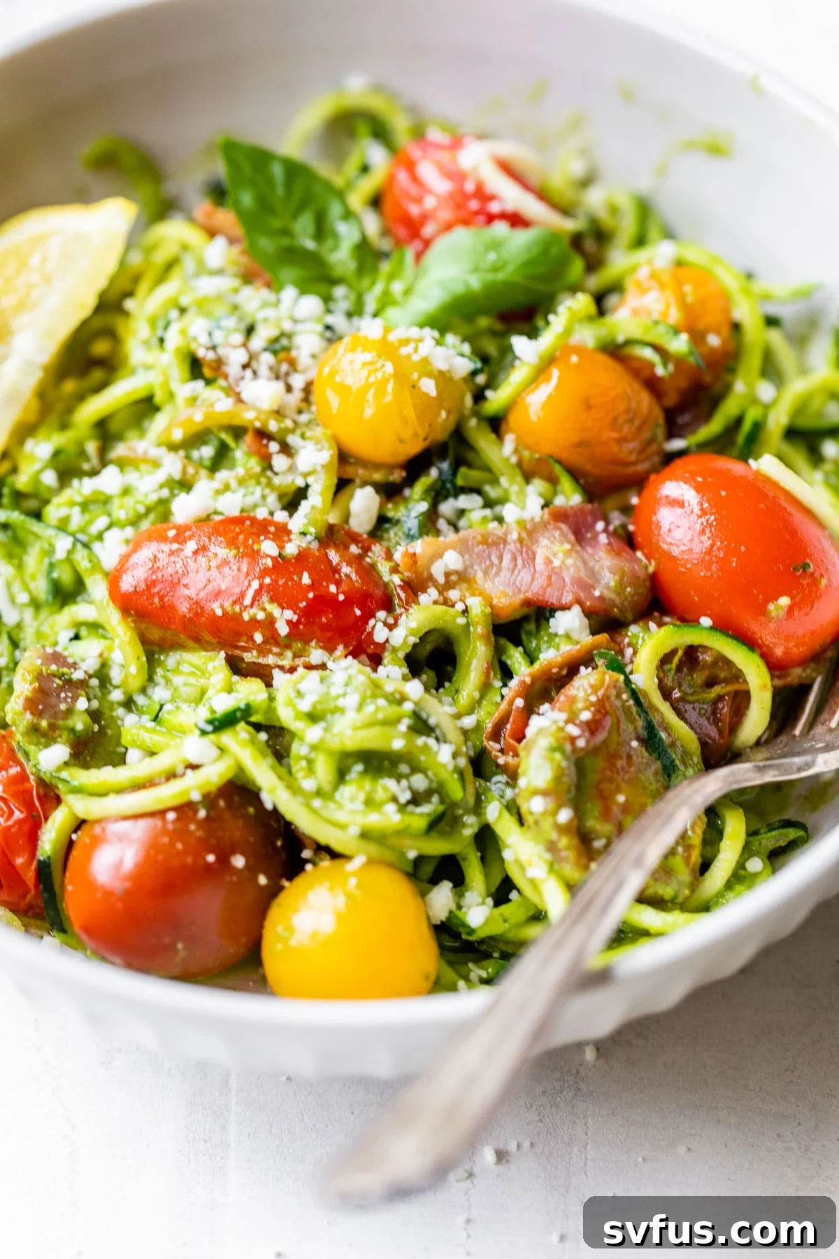close up of pesto zucchini noodles in a bowl, showcasing the rich pesto and fresh toppings