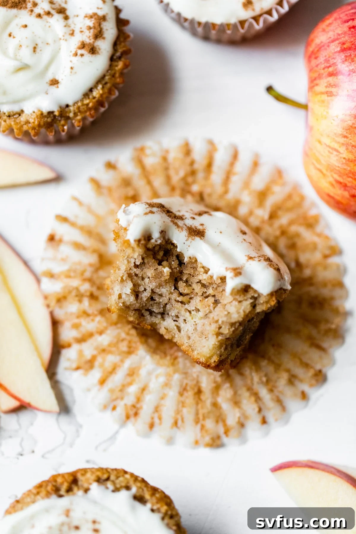 A perfectly baked gluten-free apple cupcake with a bite taken out of it, revealing its moist interior and generous, creamy icing.