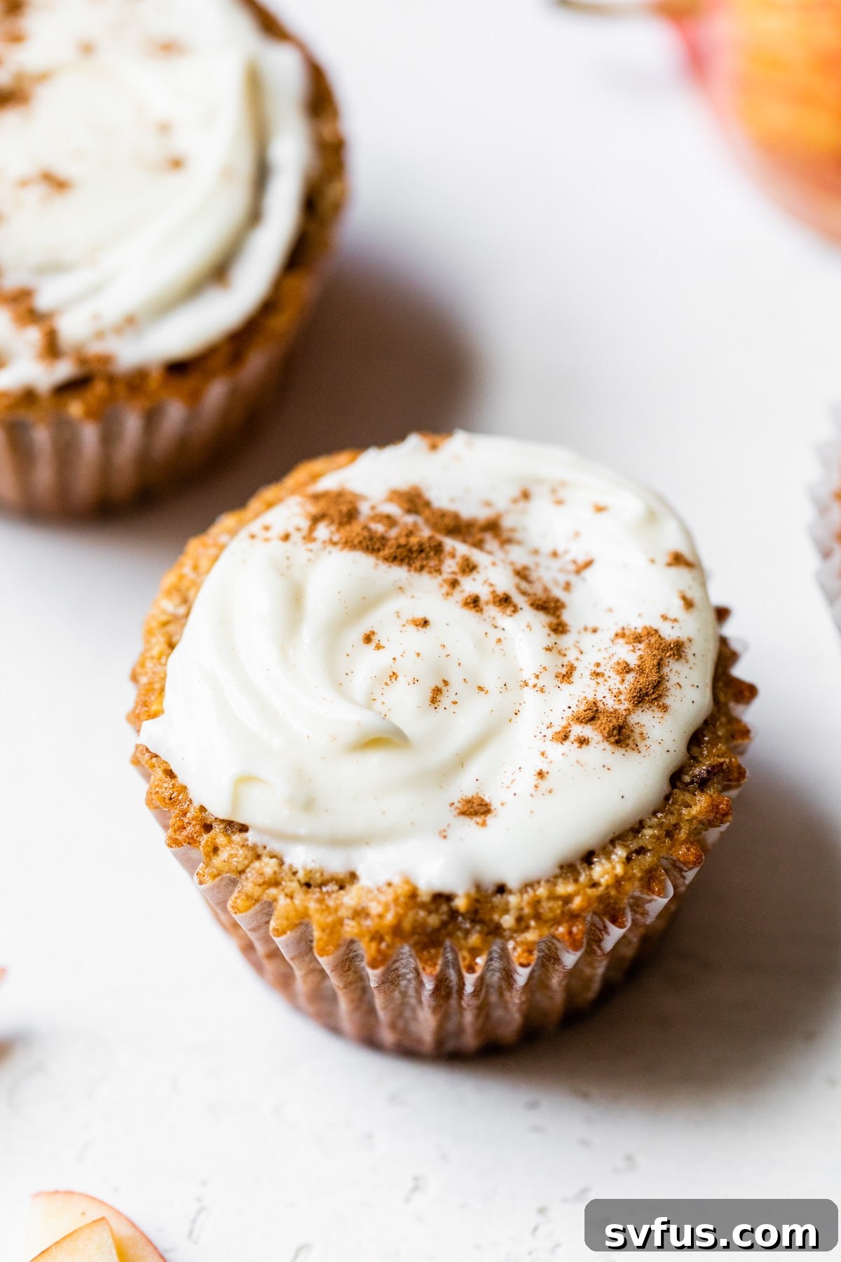 A beautifully iced gluten-free apple cupcake, elegantly topped with a dusting of cinnamon, against a softly blurred background.