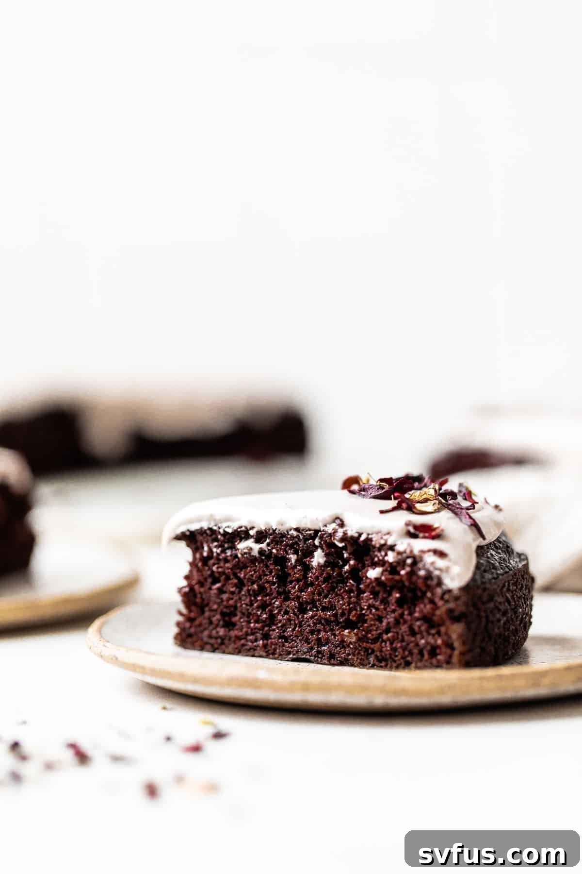 A perfectly sliced piece of vegan chocolate cake with pink hibiscus icing on a white plate.