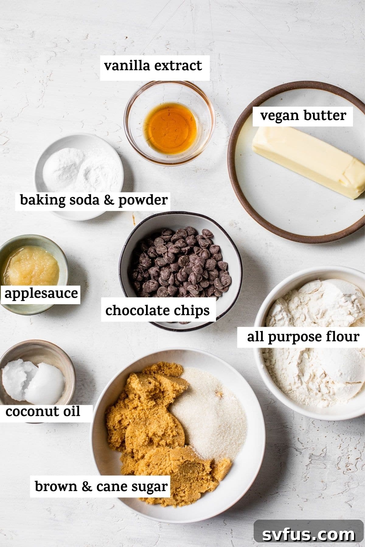 Array of vegan chocolate chip cookie ingredients laid out on a table, including flour, sugars, butter, oil, and applesauce