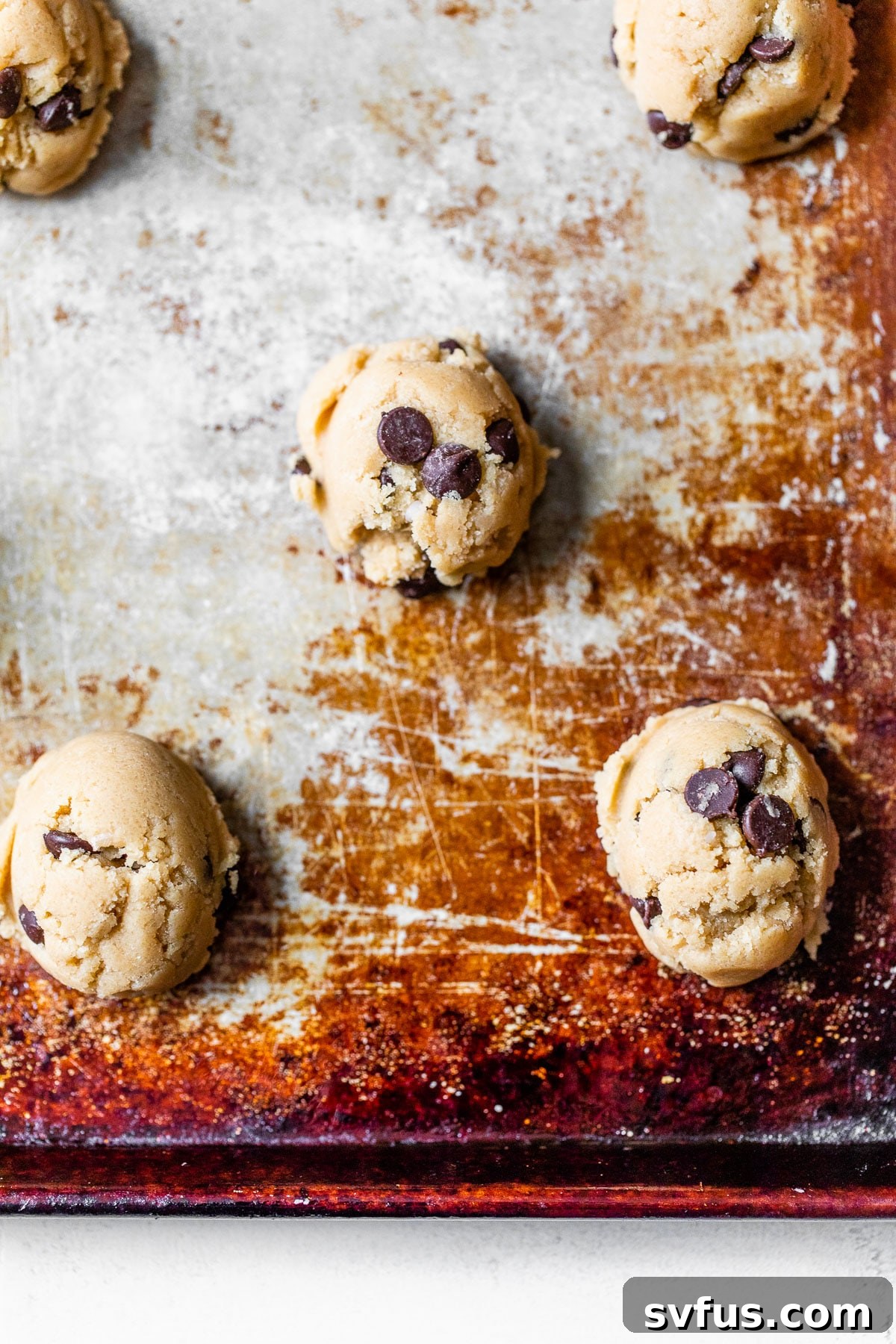 Scooped vegan chocolate chip cookie dough balls neatly arranged on a parchment-lined baking sheet, spaced for even baking
