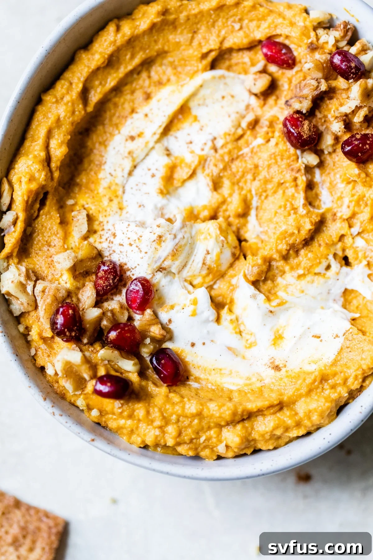 A beautifully garnished bowl of sweet pumpkin hummus with pecans and a swirl of cream cheese on top, ready to be served.
