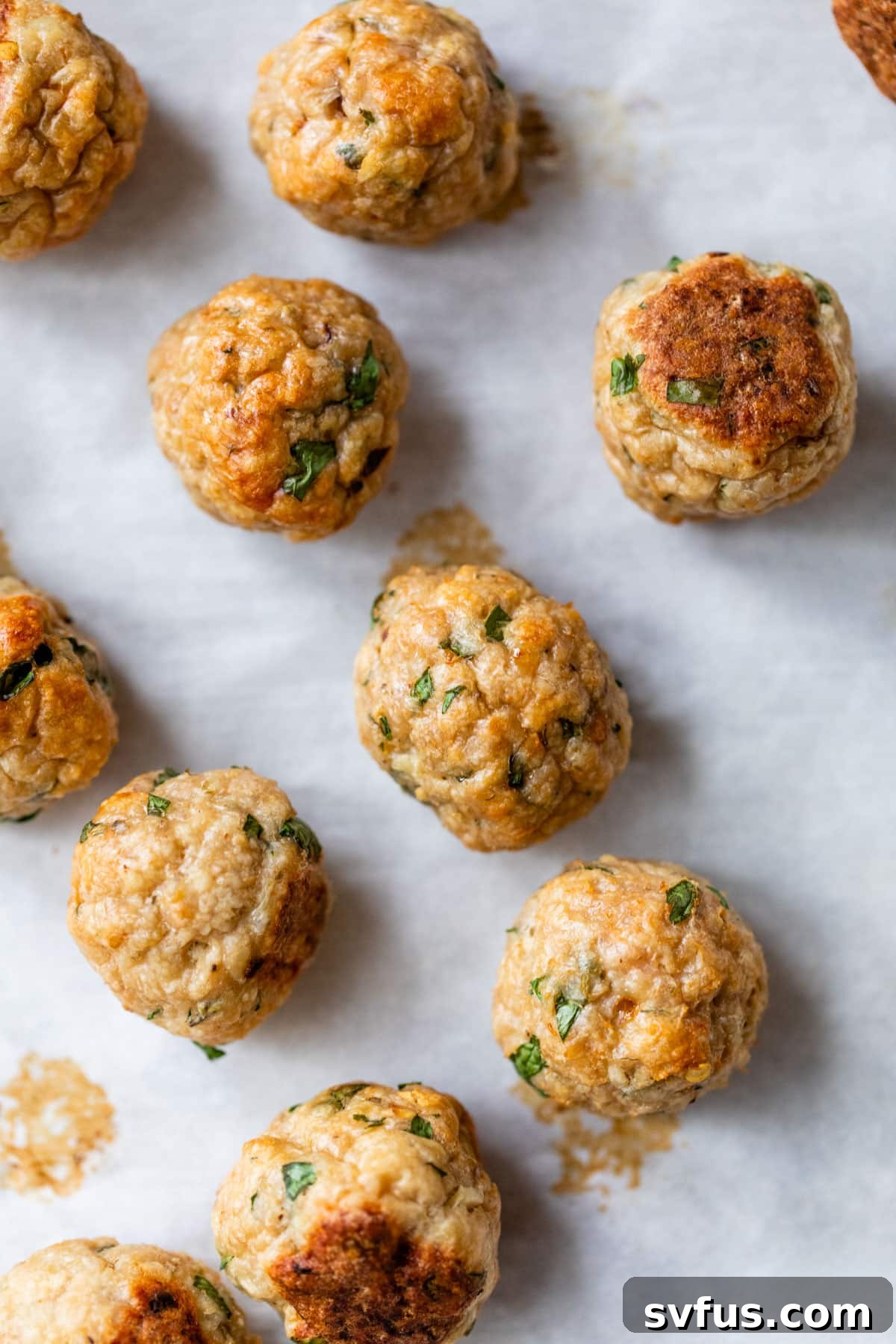 Close-up of golden-brown baked chicken meatballs on parchment paper on a baking sheet, showing their crispy exterior and even cooking.