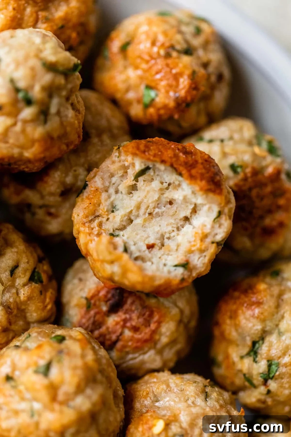 A close-up of a baked chicken meatball cut in half, revealing its juicy, perfectly cooked interior and tender texture.
