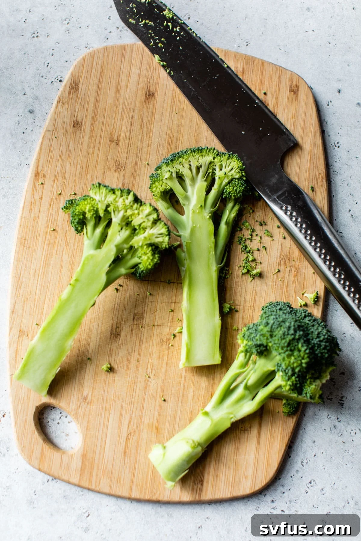 A sharp knife precisely slicing a head of broccoli vertically on a wooden cutting board, illustrating the 