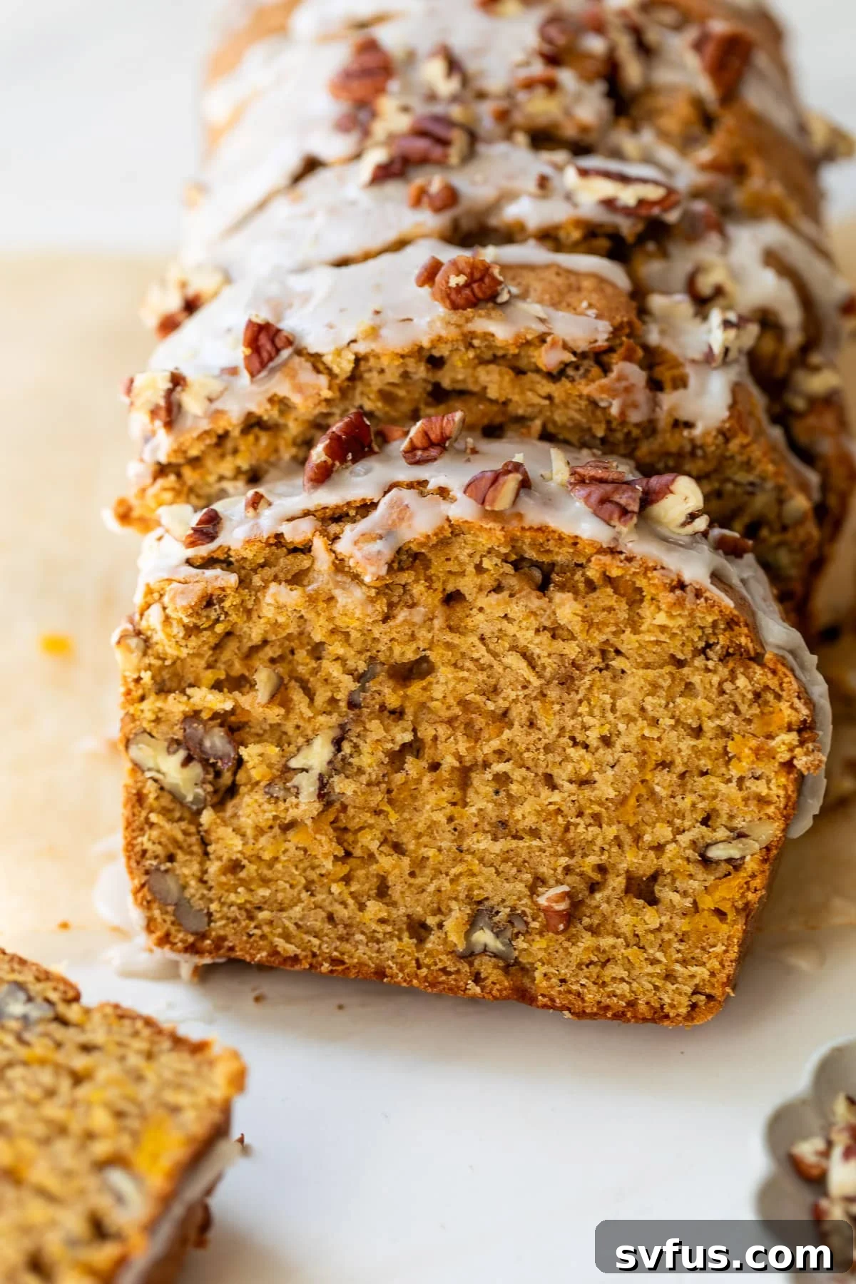 overhead view of a sliced loaf of butternut squash bread topped with a white glaze and pecans, ready to be served for a cozy fall treat.