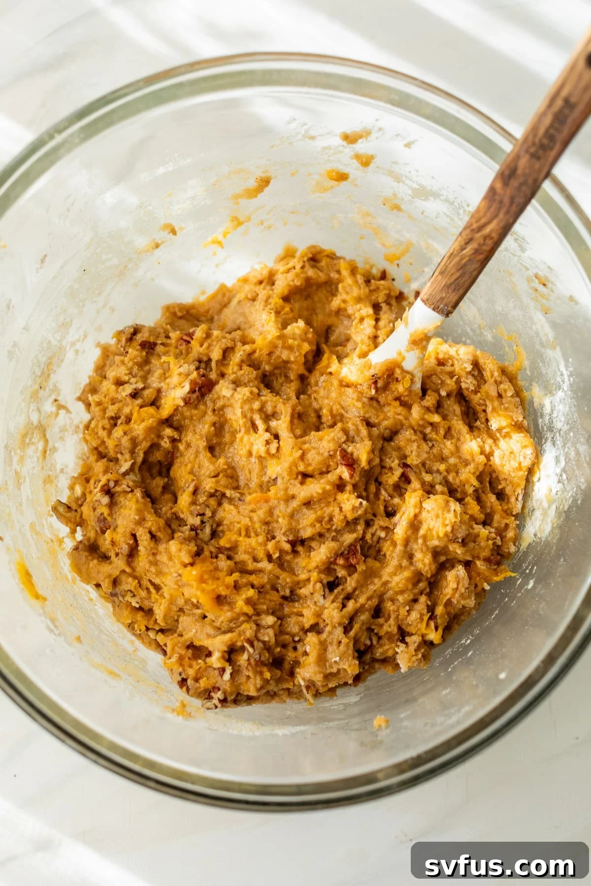 using a wooden spoon to gently stir the rich, spiced batter for butternut squash bread in a large glass bowl.
