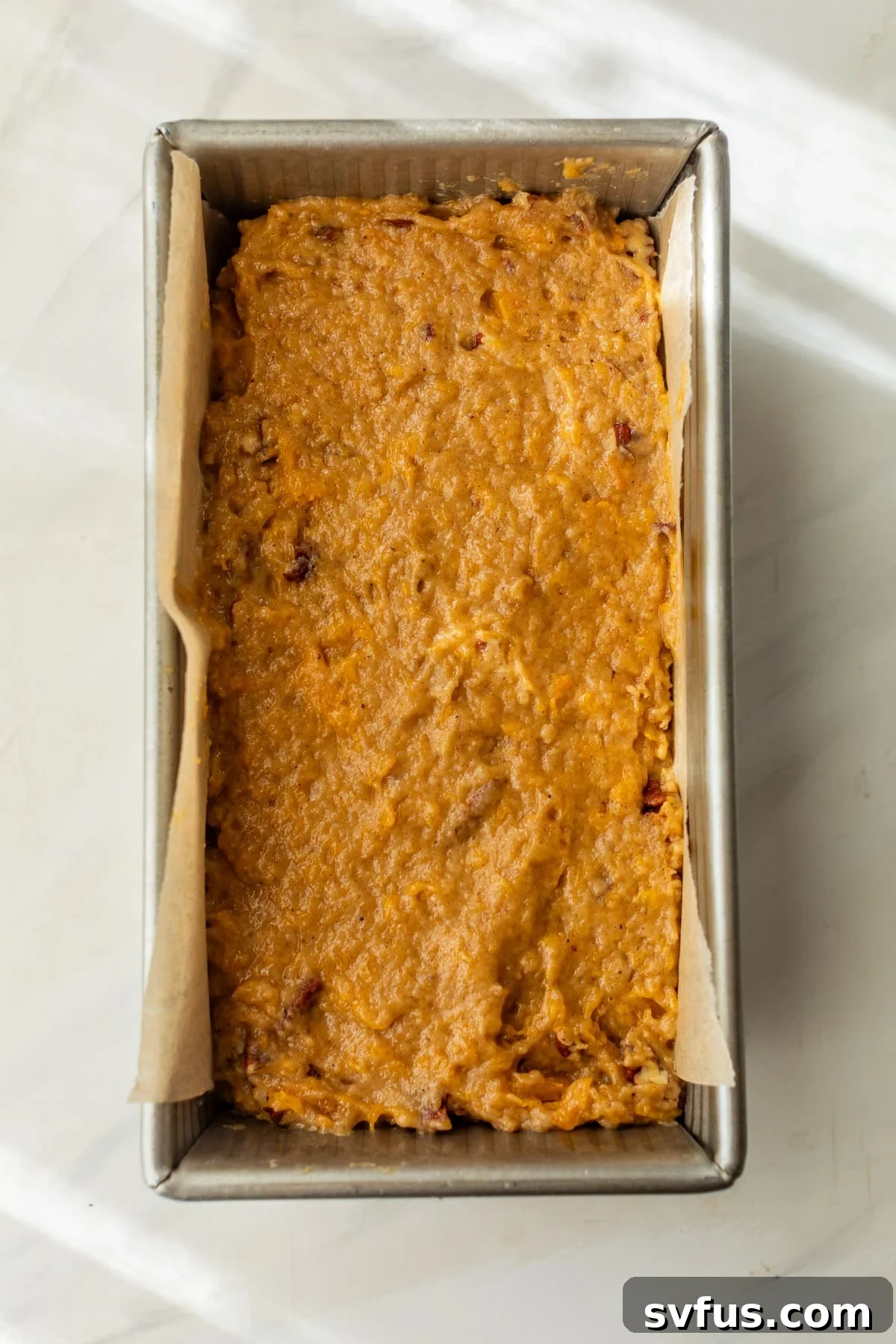 the smooth, golden batter for butternut squash bread poured evenly into a parchment-lined loaf pan, ready for baking.