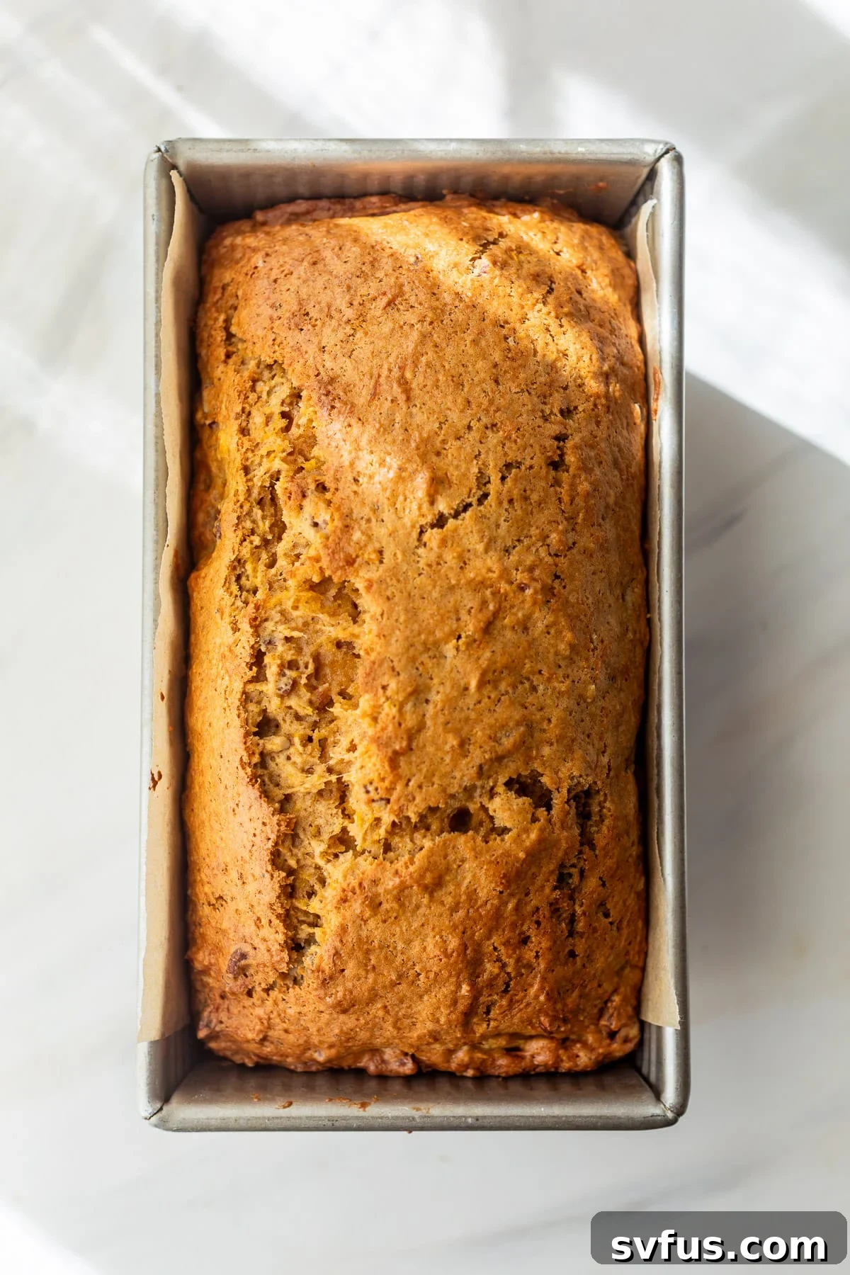 a perfectly baked loaf of butternut squash bread, golden brown and risen, resting in its loaf pan after being removed from the oven.
