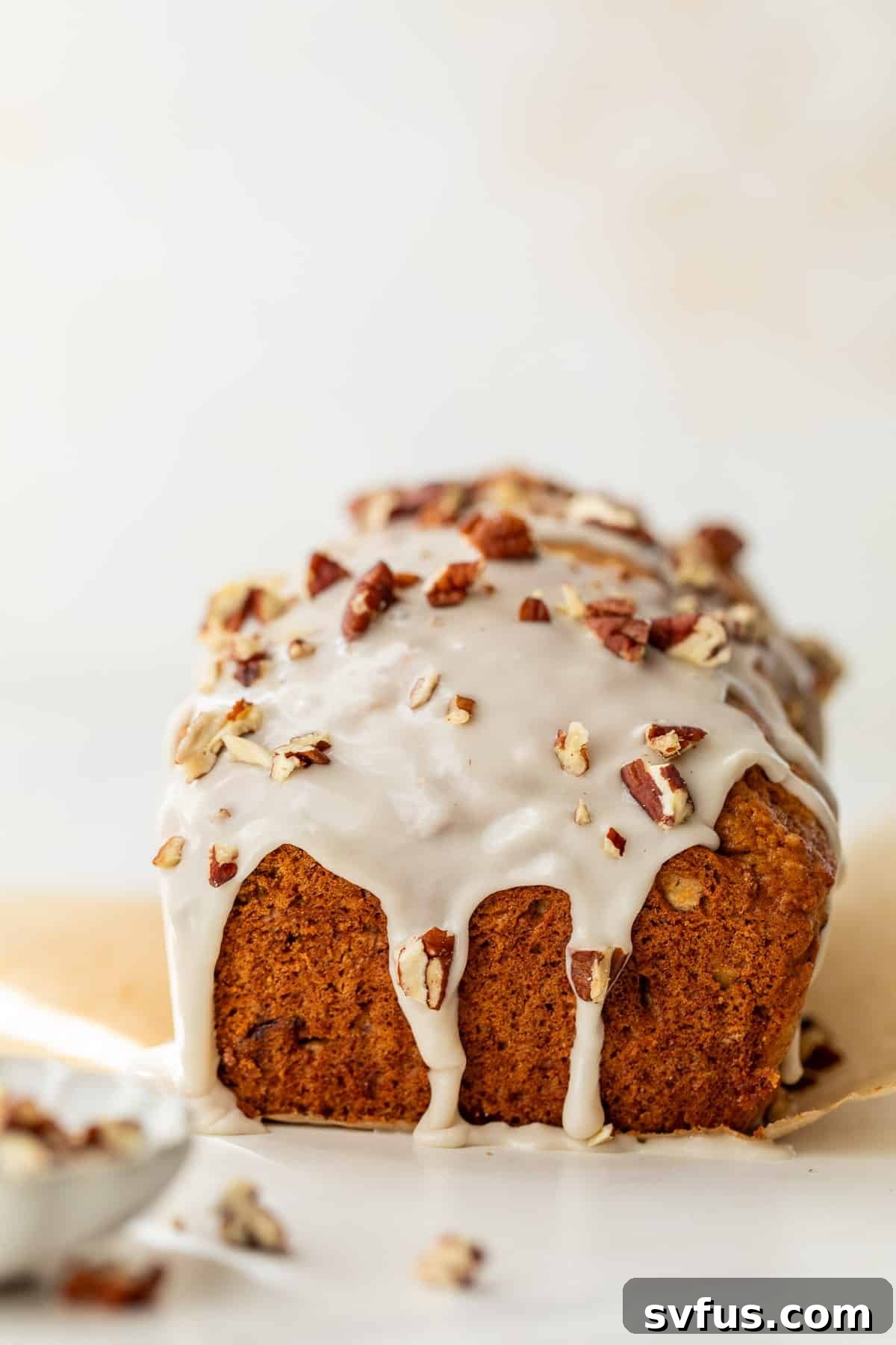 side view of a baked loaf of butternut squash bread beautifully topped with a delicate white glaze and scattered pecans, ready to be sliced.