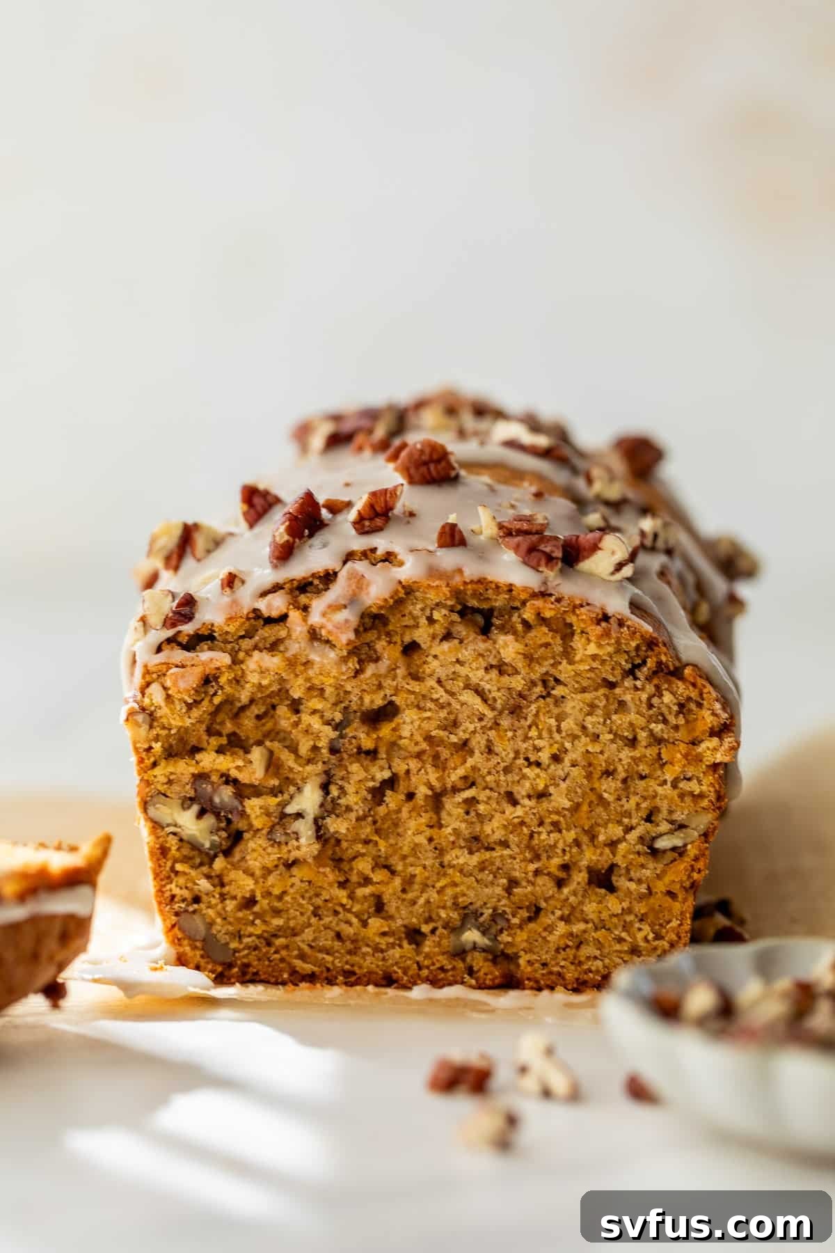 side view of a sliced loaf of butternut squash bread topped with a white glaze and pecans, showcasing its beautiful crumb, stored on a cutting board.