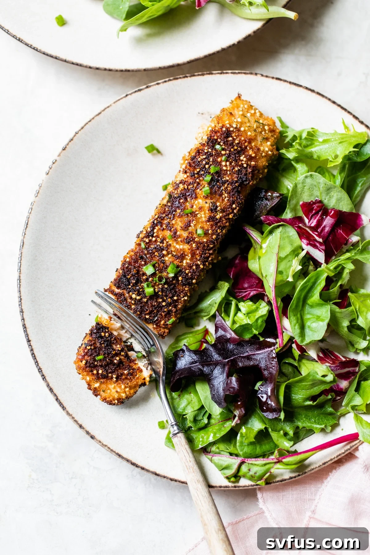 A beautifully plated Quinoa Crusted Salmon fillet, served alongside a vibrant green salad, resting on a rustic wooden table.