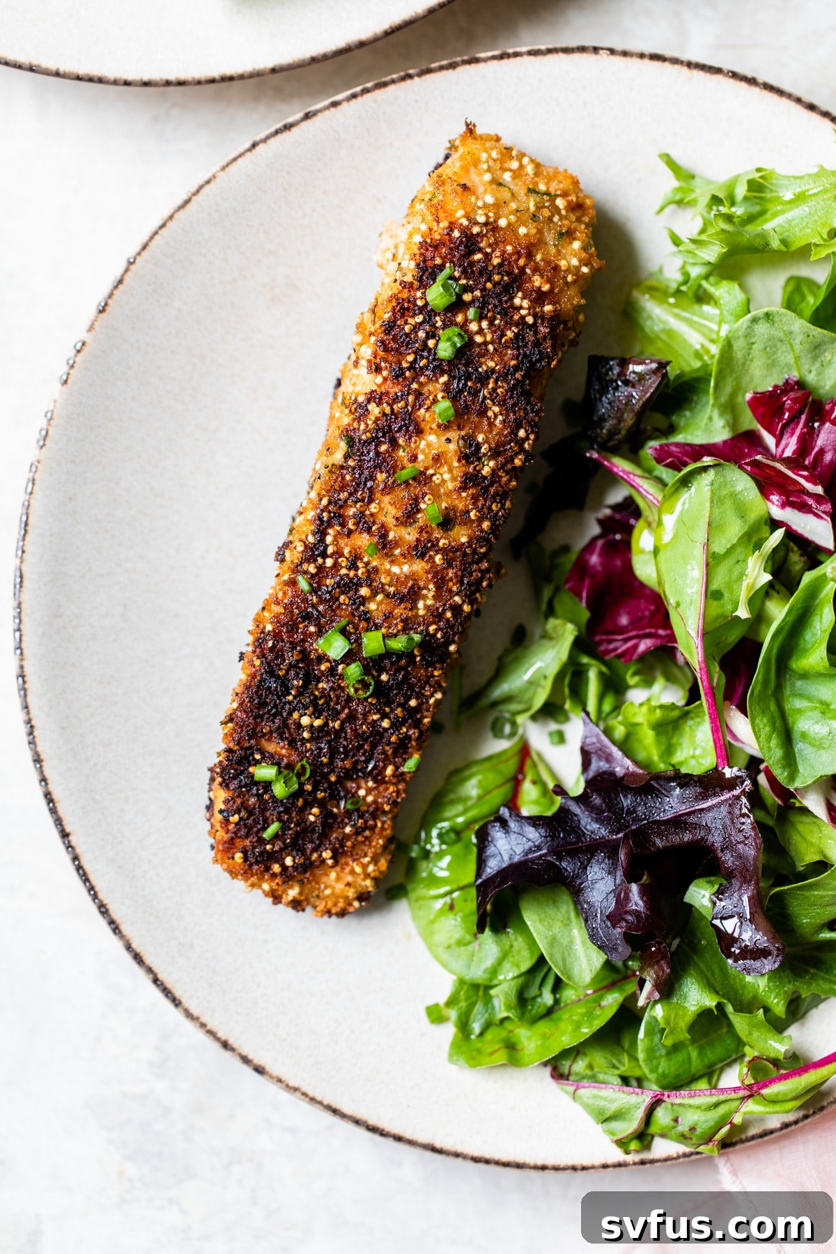 A vibrant plate featuring Quinoa Crusted Salmon, garnished with fresh chives, and served with a colorful medley of fresh greens and vegetables.