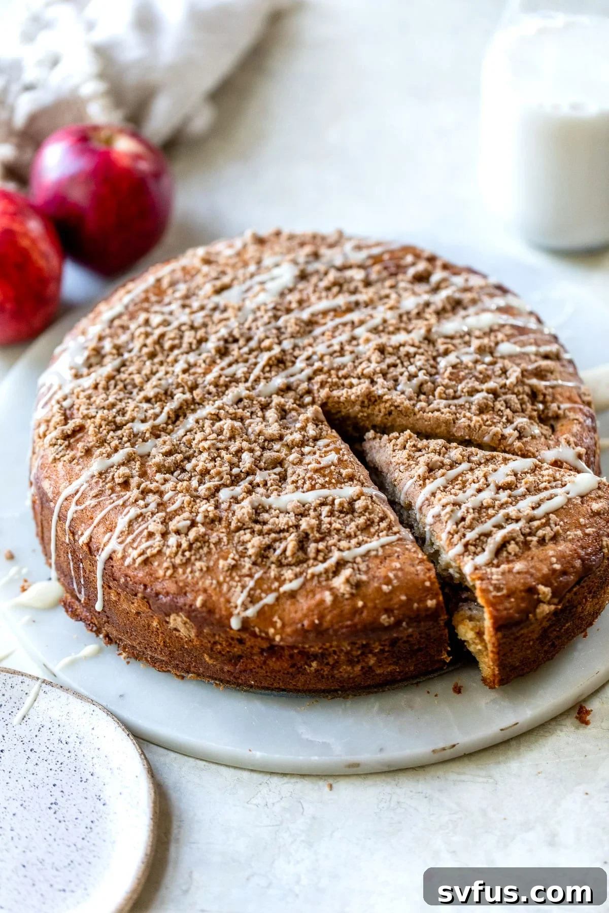 A round coffee cake with a generous crumb topping displayed on an elegant marble platter, ready to be served.
