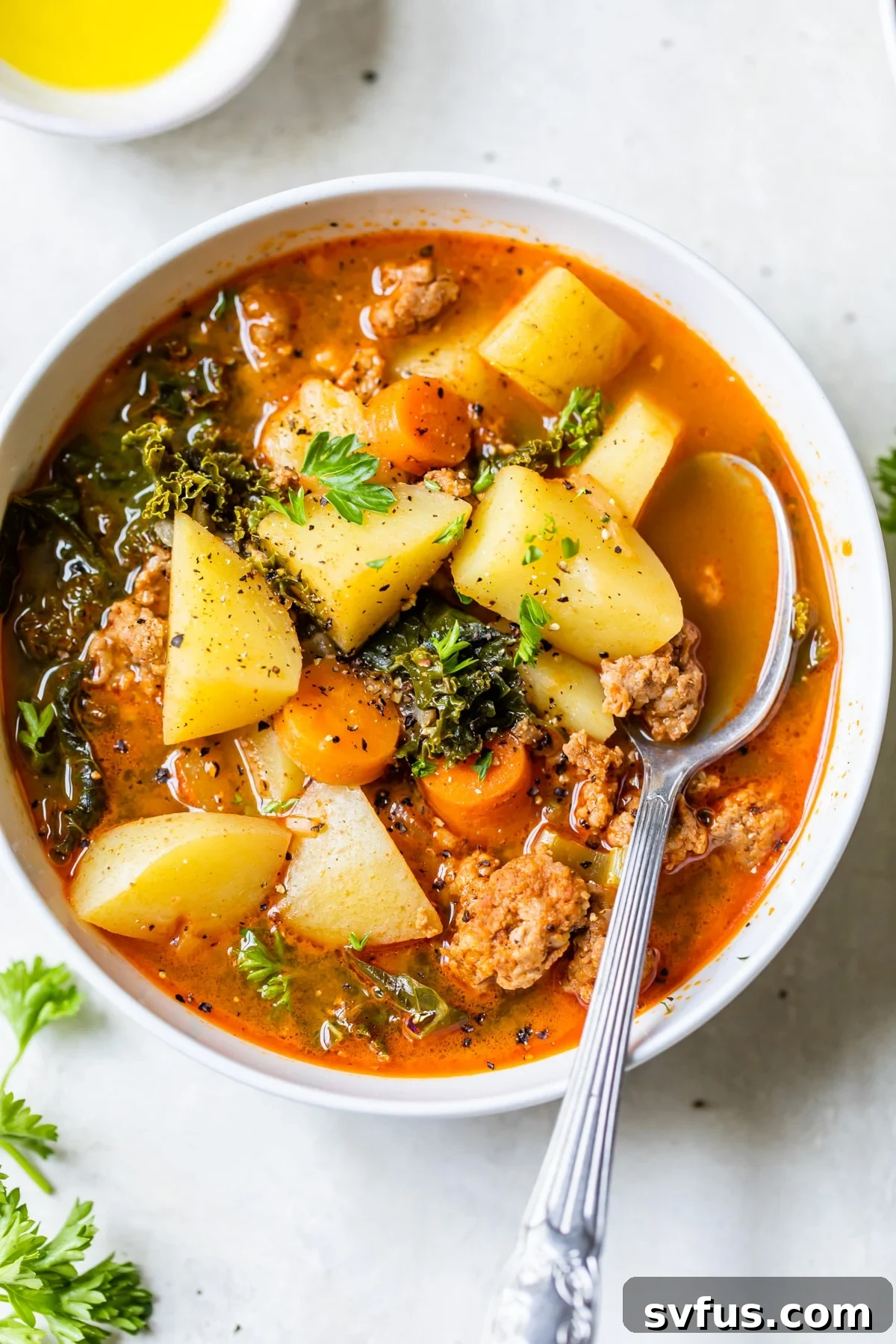 A steaming bowl of Spicy Sausage Potato Soup with chunks of sausage, potato, and kale, garnished with fresh herbs, ready to be enjoyed.