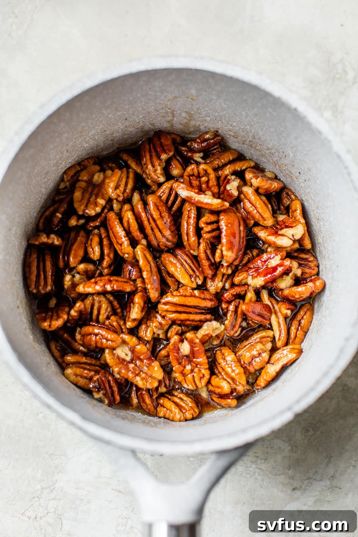 Pecans simmering in a saucepan with maple syrup and butter.