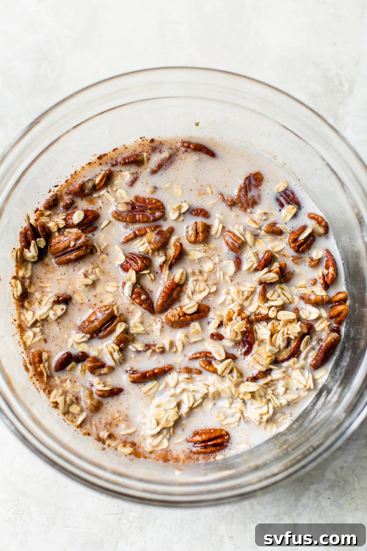 Oats, milk, and glazed pecans combined in a large glass bowl, ready for baking.