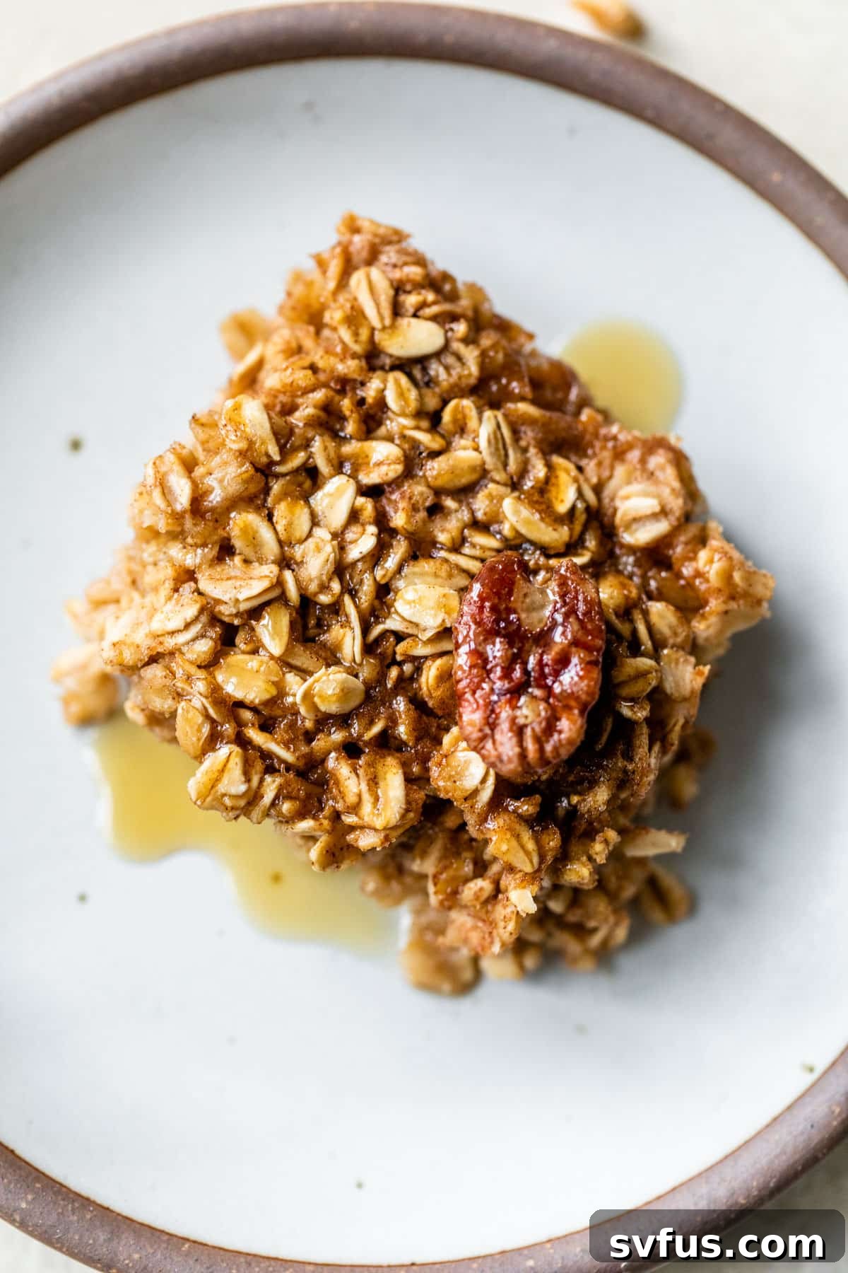 A slice of pecan pie baked oatmeal, topped with a whole pecan and a drizzle of maple syrup.