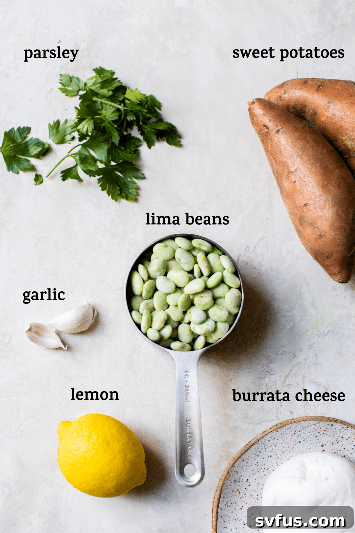 Overhead shot of fresh ingredients on a wooden table, featuring vibrant lima beans, diced sweet potatoes, garlic cloves, and a ball of burrata cheese, hinting at the delicious salad to come.