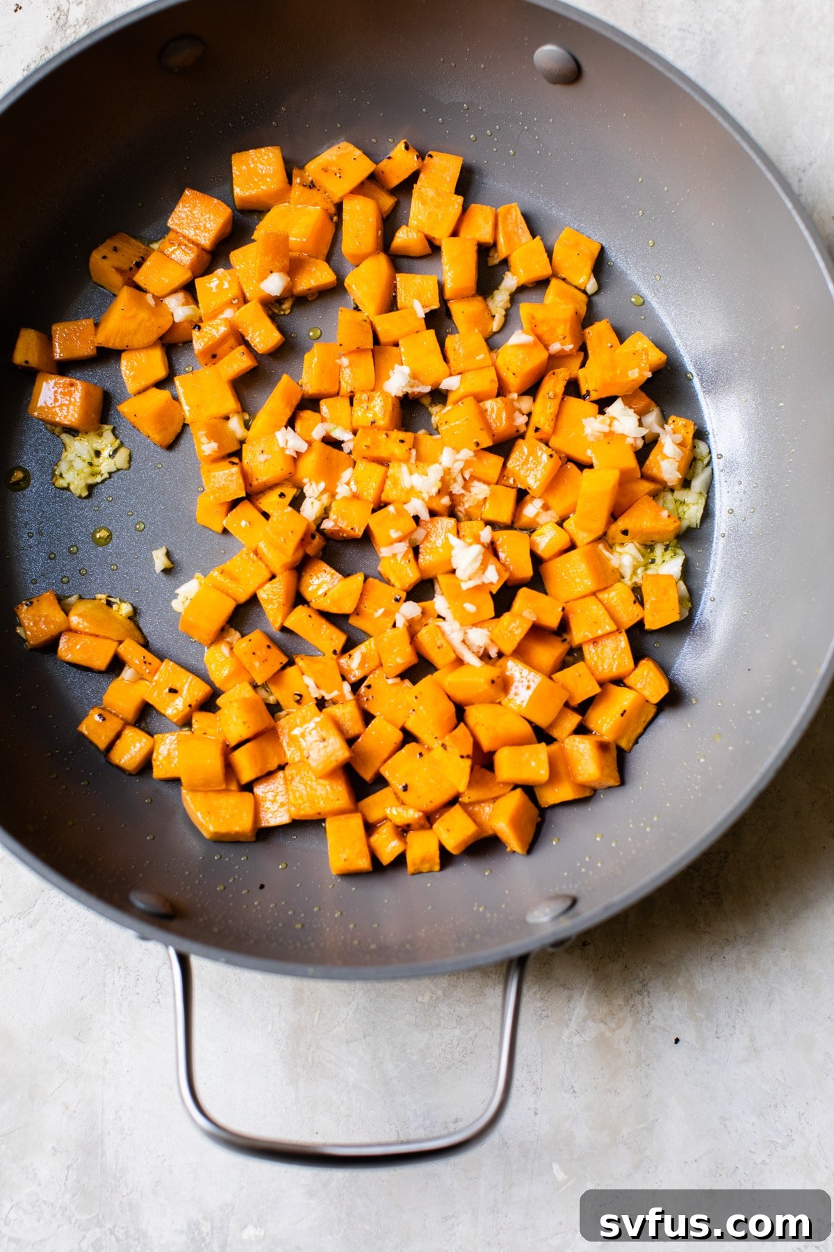 Diced sweet potatoes and minced garlic sizzling in a hot skillet with olive oil, beginning to soften and caramelize.