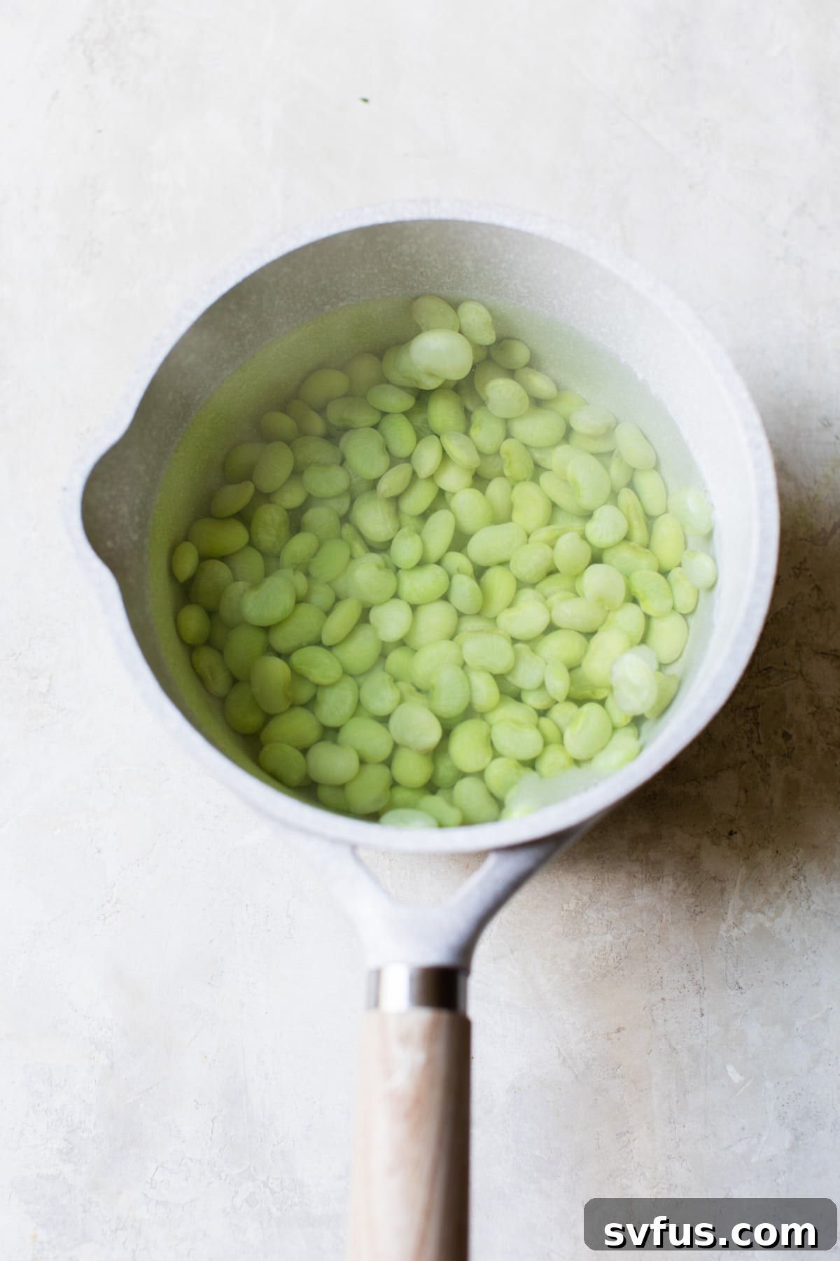 Vibrant green lima beans simmering in a saucepan of boiling water, steam rising, indicating they are nearly cooked to perfection.