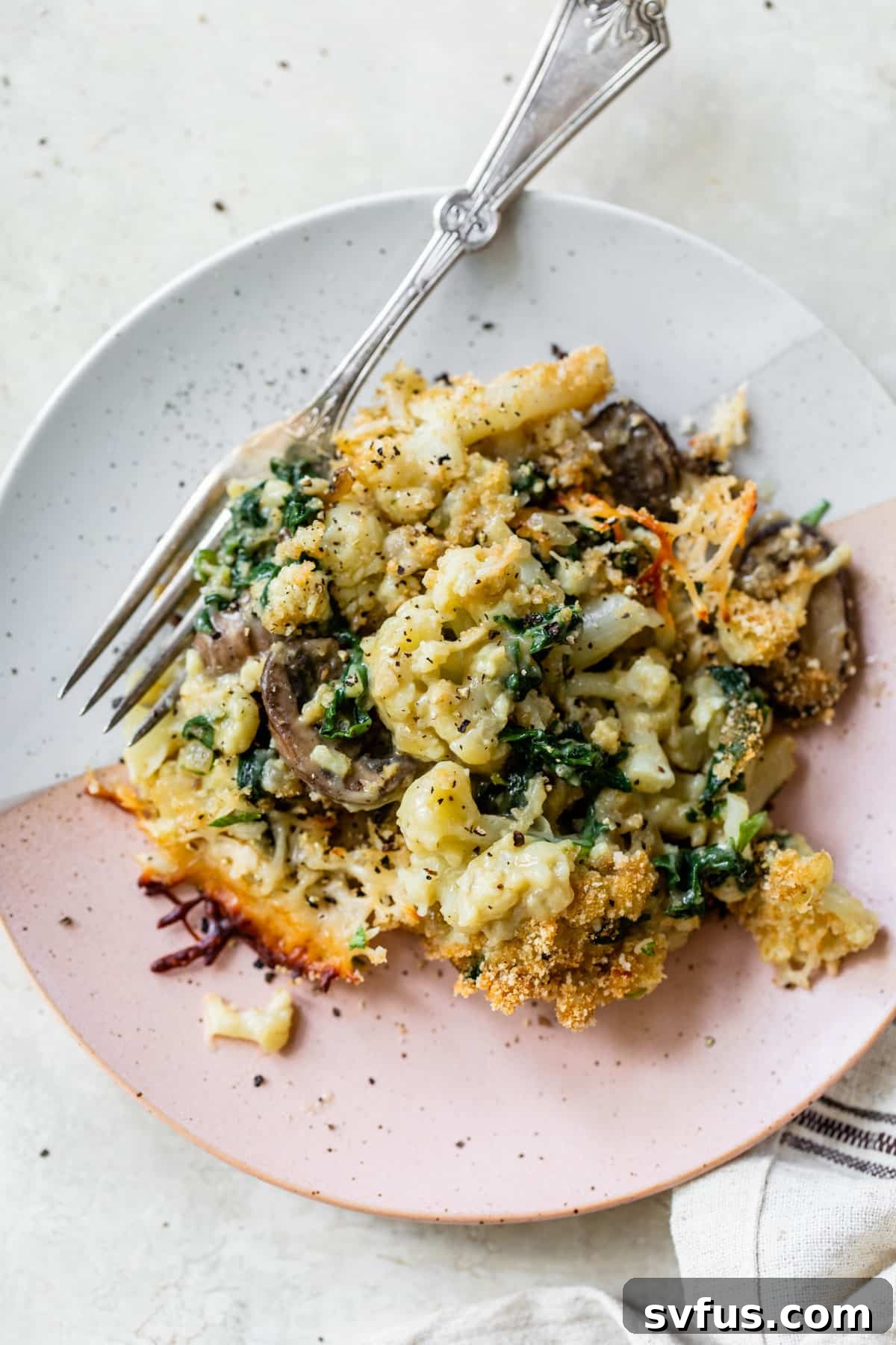 A small plate showcasing a serving of cooked vegan cauliflower gratin with mushrooms and spinach, garnished with fresh parsley.