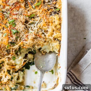 A golden brown vegan cauliflower gratin in a casserole dish, topped with crispy breadcrumbs and a spoon ready to serve.